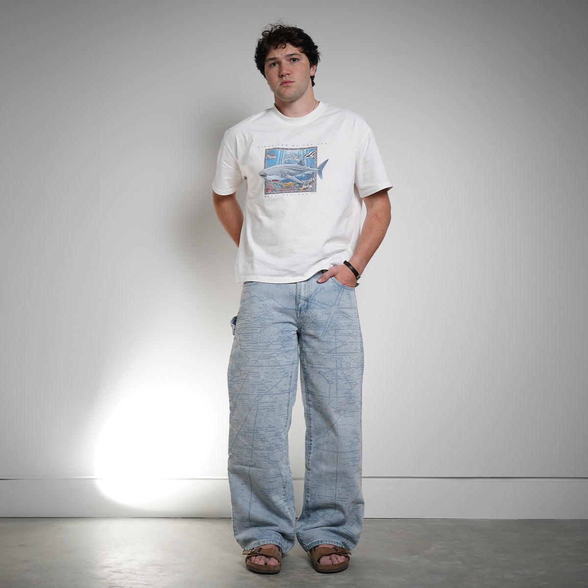 Model wearing Grand Line Pants in light blue map-print denim with a white tee, front view