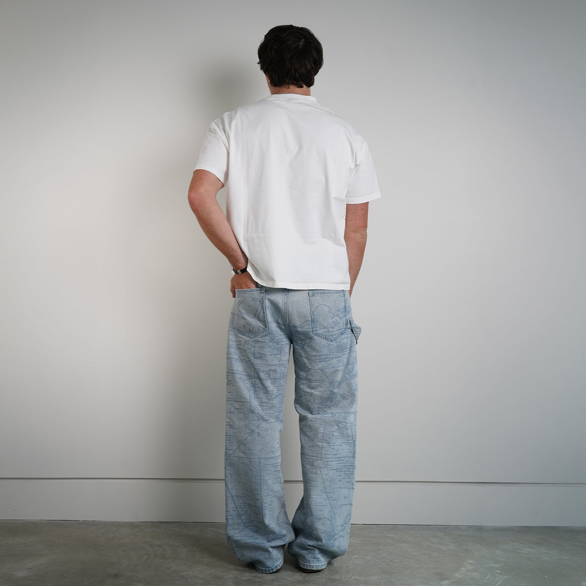 Model wearing Grand Line Pants in light blue map-print denim with a white tee, back view