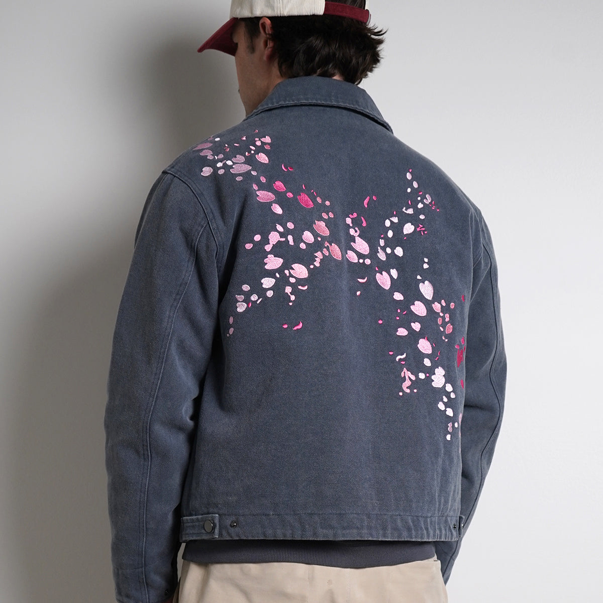 Washed navy Drum Island Jacket with scattered pink petals, partially zipped, back view on model