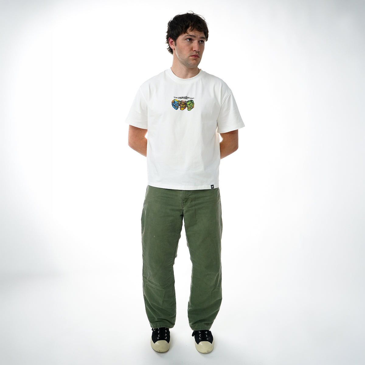 Man wearing a white t-shirt with a graphic design and green pants on a white background