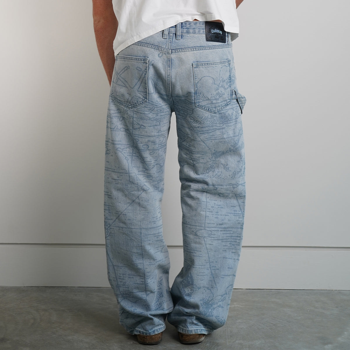 Model wearing Grand Line Pants in light blue map-print denim with a white tee, back view