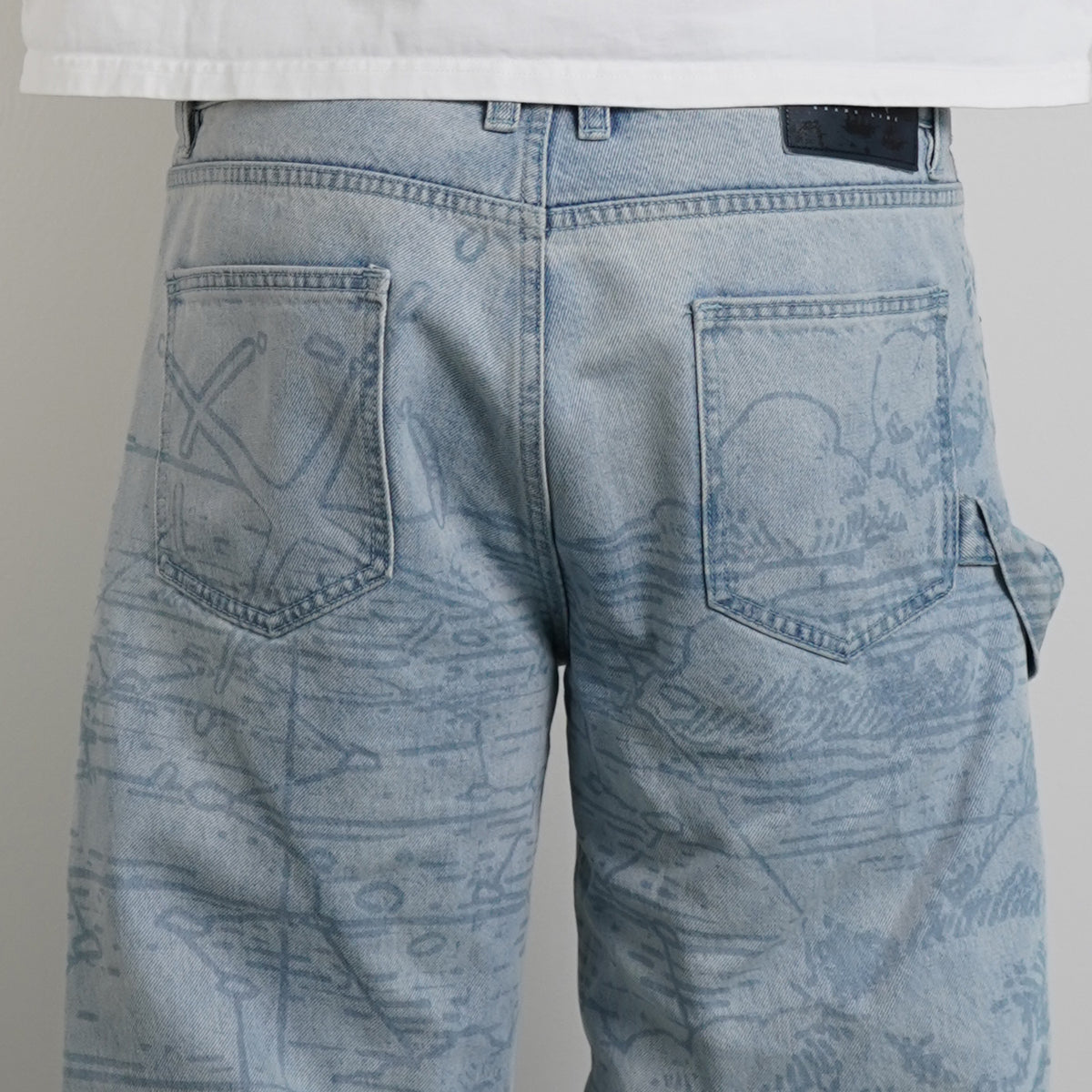 Model wearing Grand Line Pants in light blue map-print denim with a white tee, close up back view