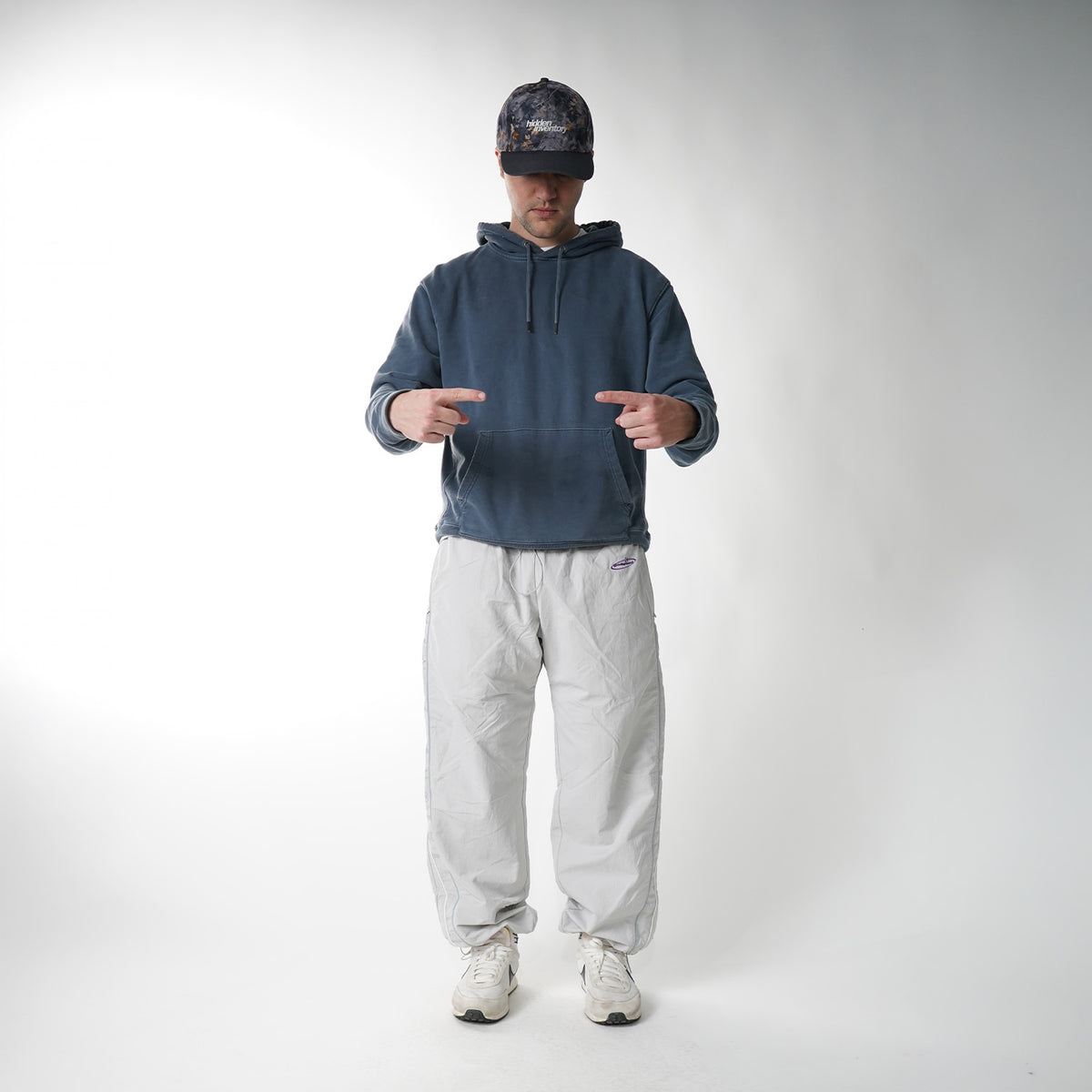 Person wearing a blue hoodie, light gray pants, and a cap on a white background