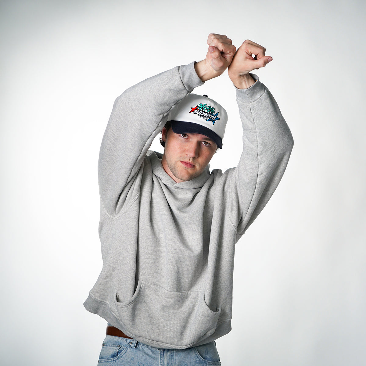 Person wearing a gray hoodie and a cap with a logo on a white background