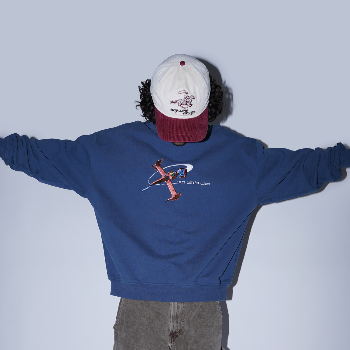 Person wearing a blue sweatshirt with a graphic design and a white and red cap on a plain background