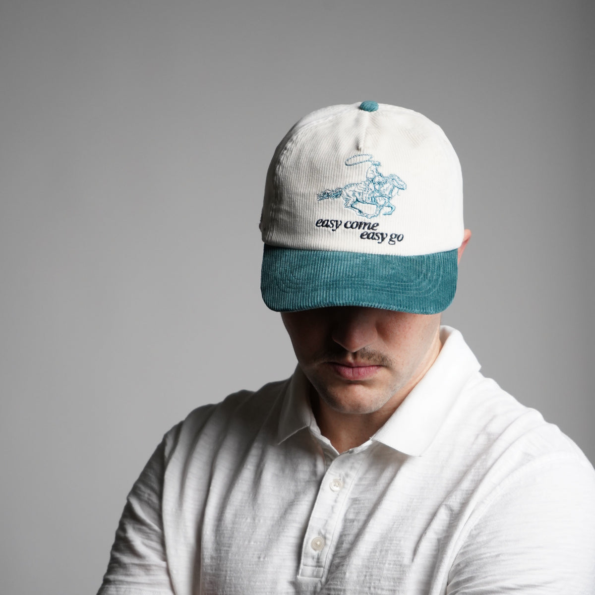 Person wearing a white shirt and teal beanie with a logo on a gray background