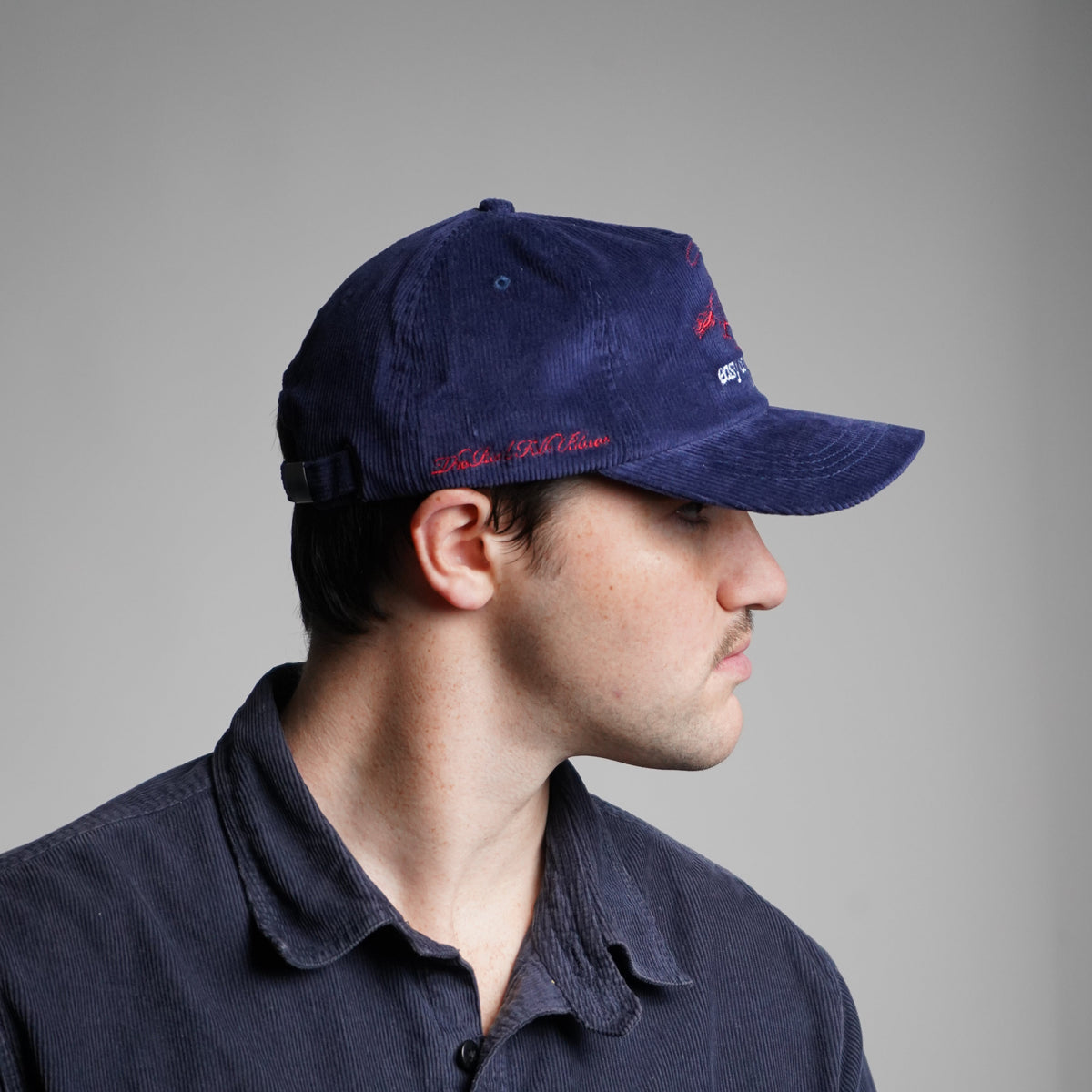 Person wearing a dark jacket and blue cap with red text on a gray background