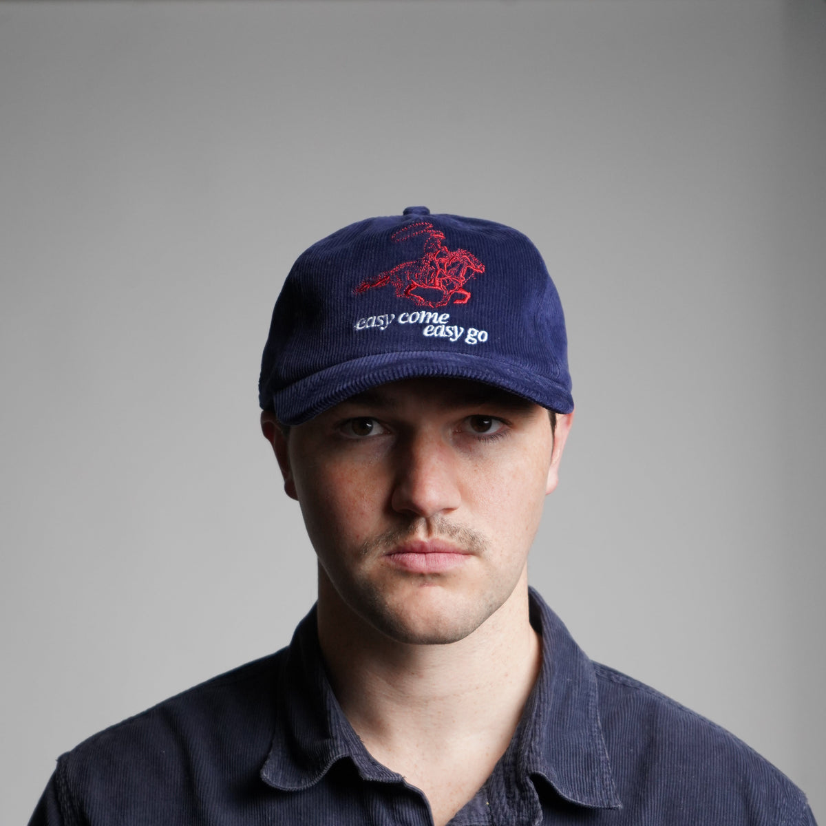Person wearing a dark jacket and a blue cap with a logo on a gray background