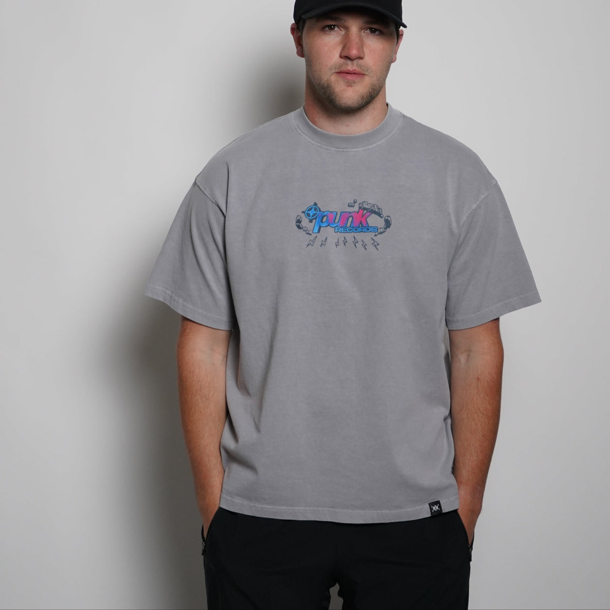Person wearing a gray t-shirt with a logo and a black cap on a plain background