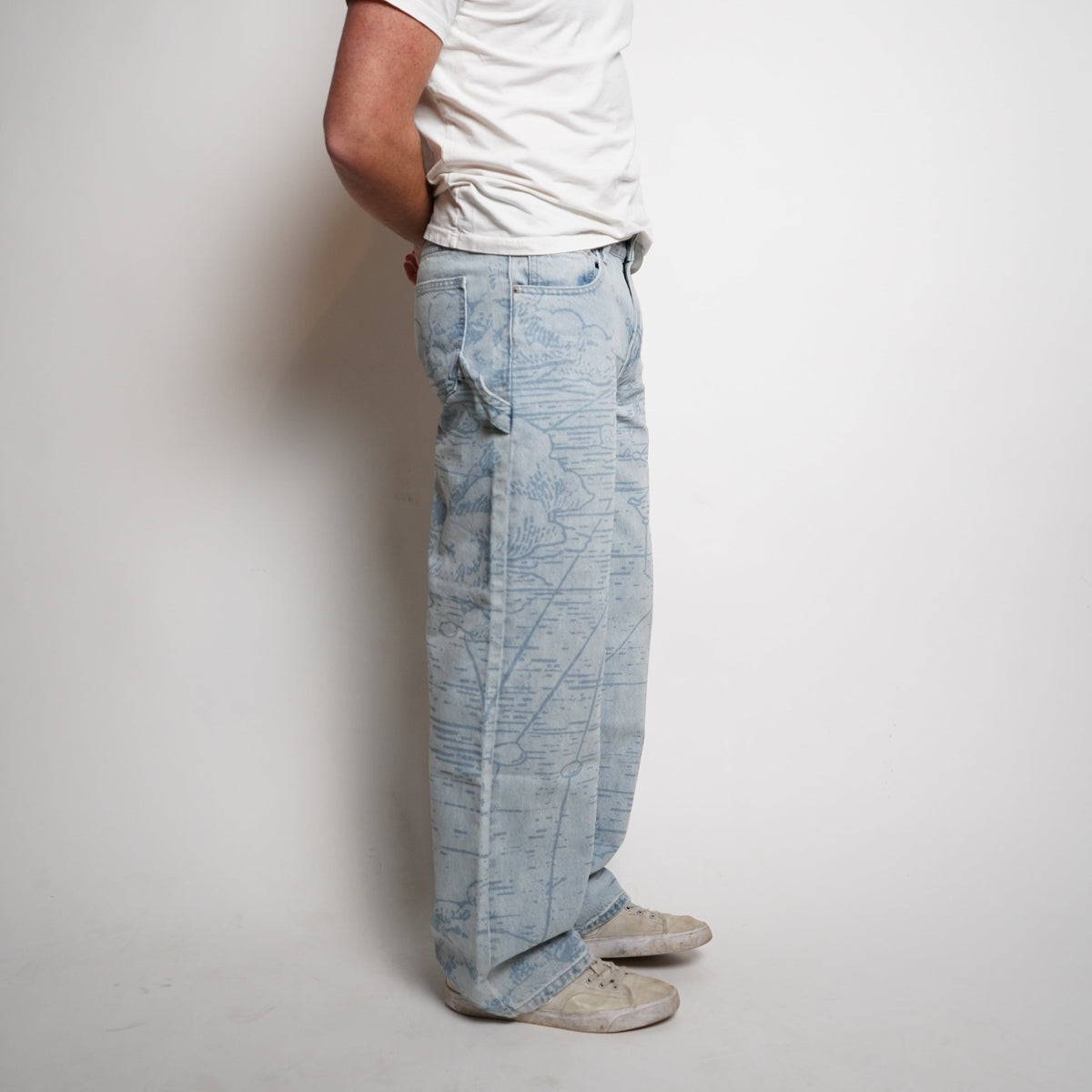Person wearing a white t-shirt, light blue jeans, and a cap on a plain background