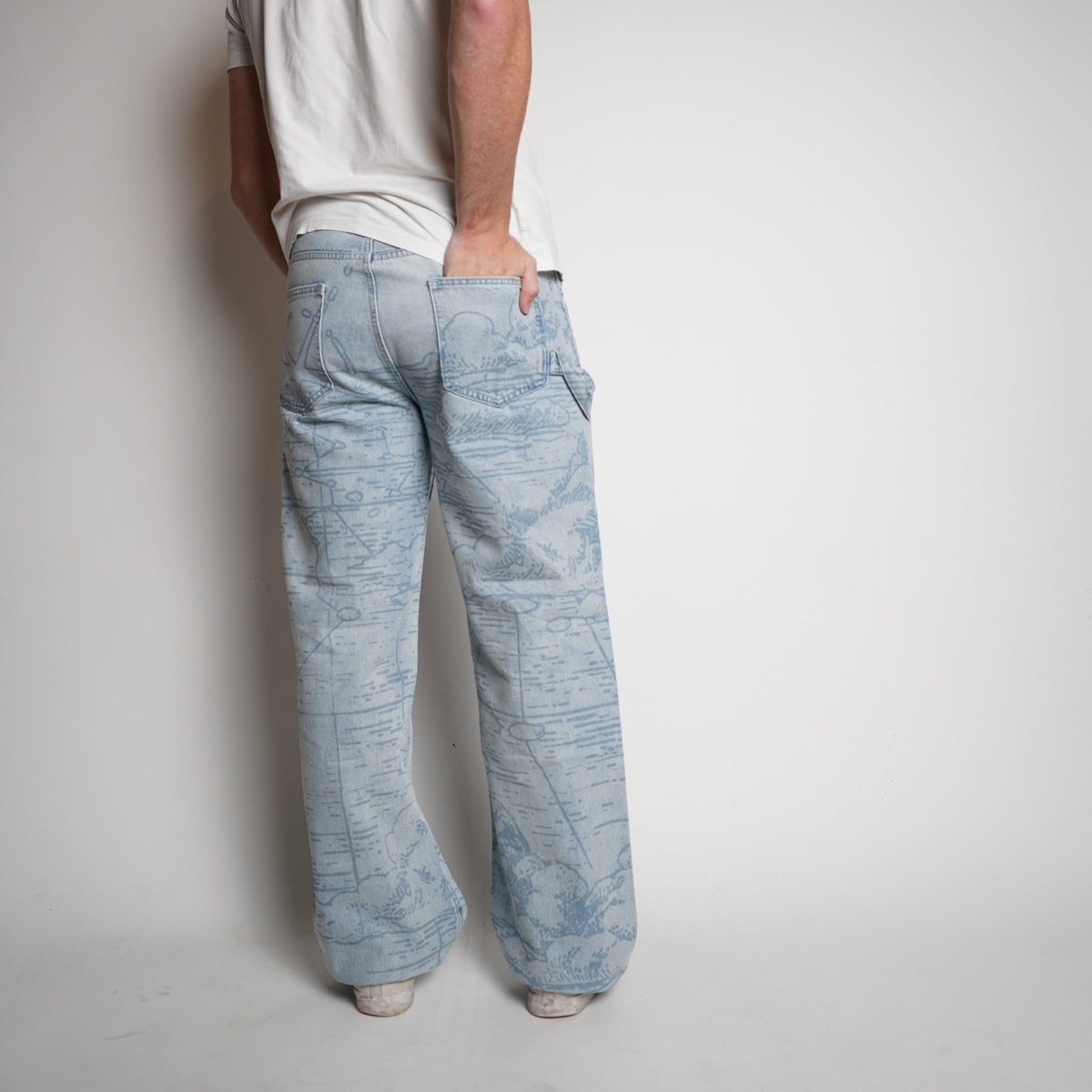 Person wearing a white t-shirt, light blue jeans, and a dark cap on a plain background