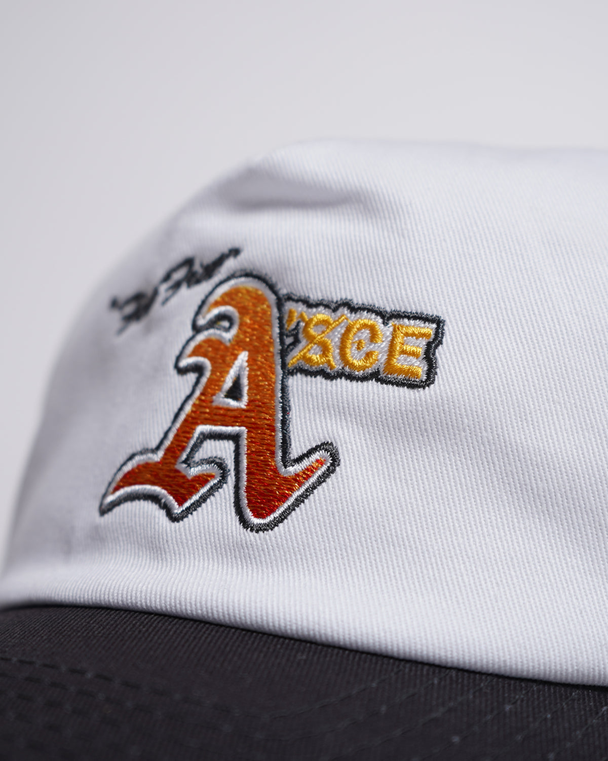 White Fire Fist Hat with orange embroidered graphic and gold text detail, close-up side view