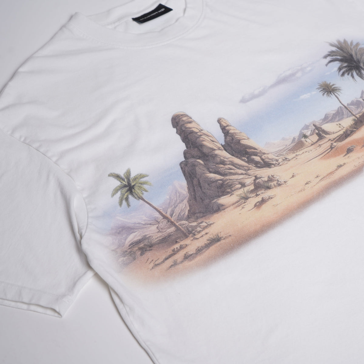White t-shirt with a desert landscape and palm tree design, featuring the word 'Alabasta'.