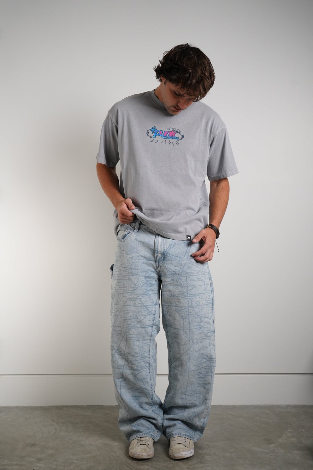 A man wearing a light gray graphic t-shirt and light blue marled sweatpants, standing against a plain light gray wall.