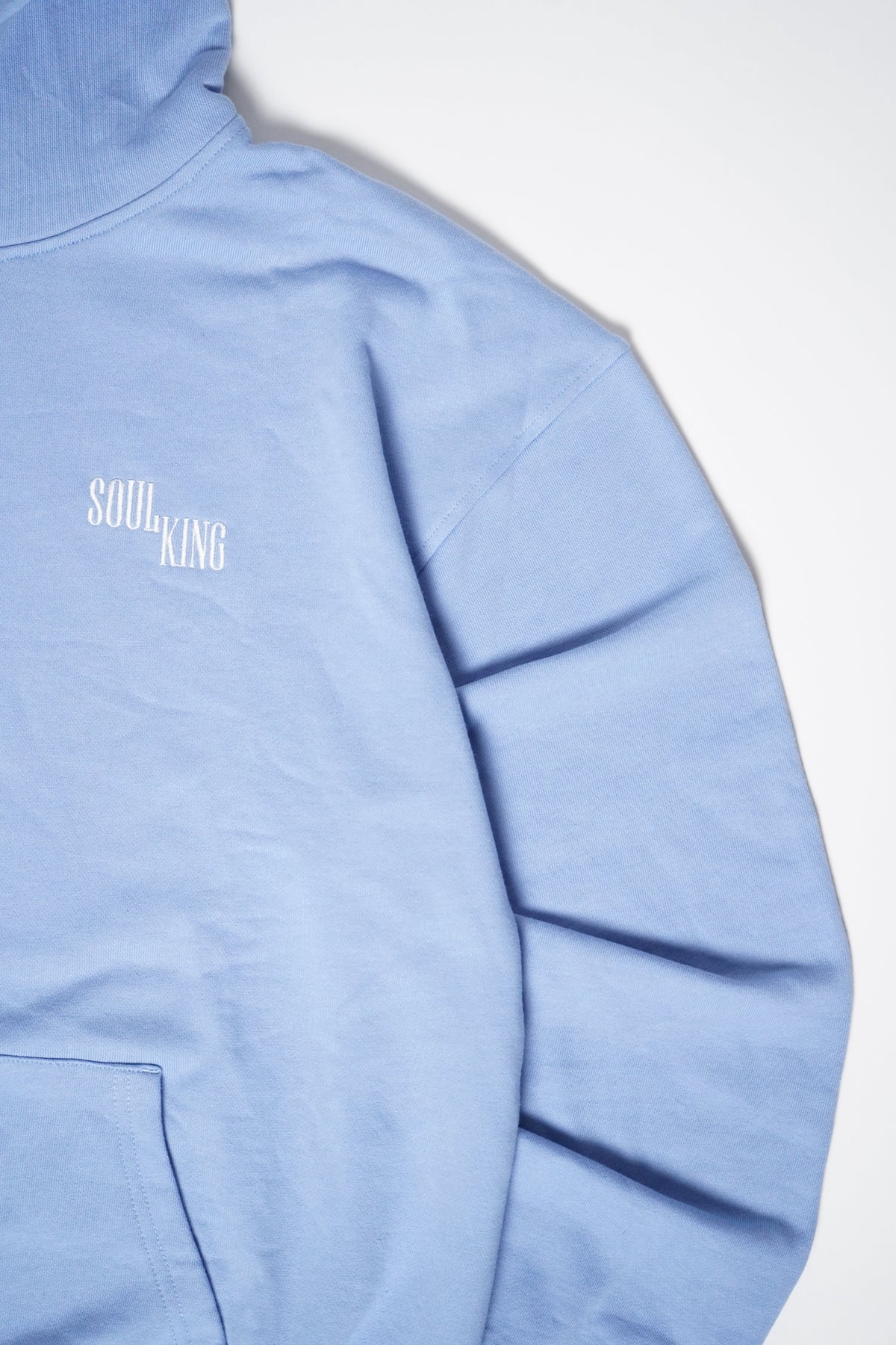 A close-up of a light blue hoodie showing the left chest area with a white 'SOUL KING' graphic logo, set against a plain light gray background.