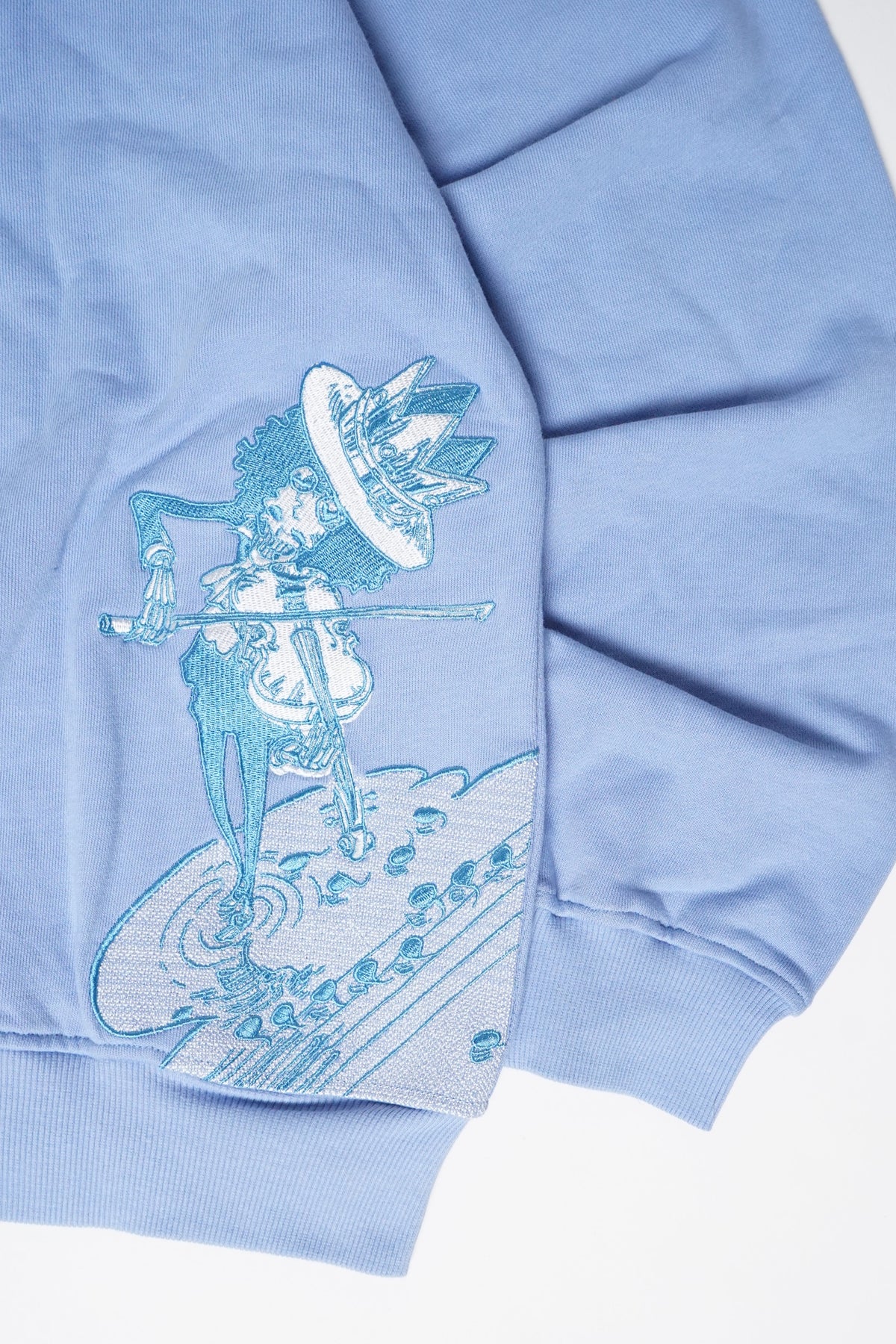 A close-up of a light blue sweatshirt featuring a light blue graphic print of a skeleton playing a violin.