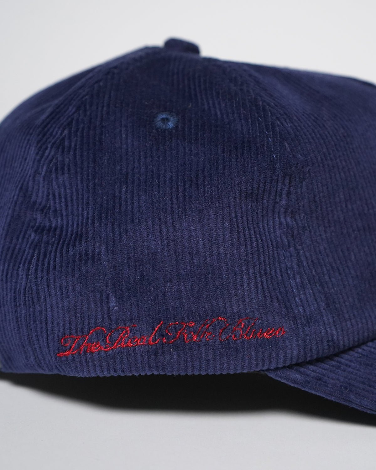 Close-up of the back of the Midnight Blue Easy Come Easy Go Hat in ribbed corduroy, with a small eyelet and red embroidered script text near the bottom edge