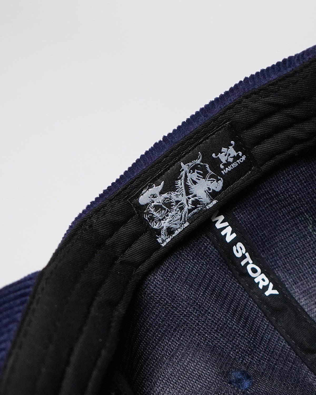 Close-up of the interior of a dark navy blue cap, showing the padded black underbrim, mesh lining, and printed black labels with white text including 'STORY' and 'HAKISTOP'.