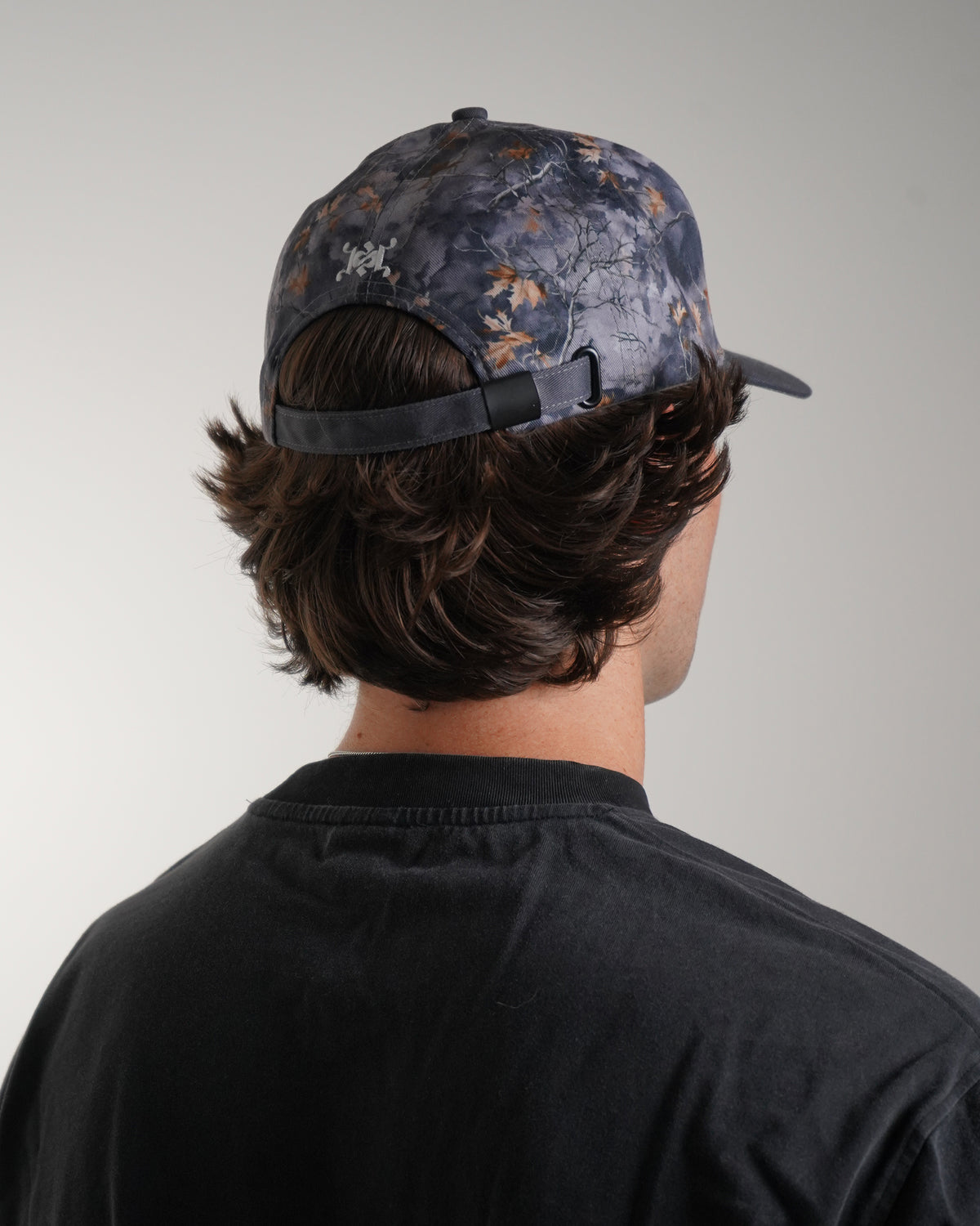 Gray leaf-camo Hidden Inventory Hat with white embroidered logo, back view showing adjustable strap in model