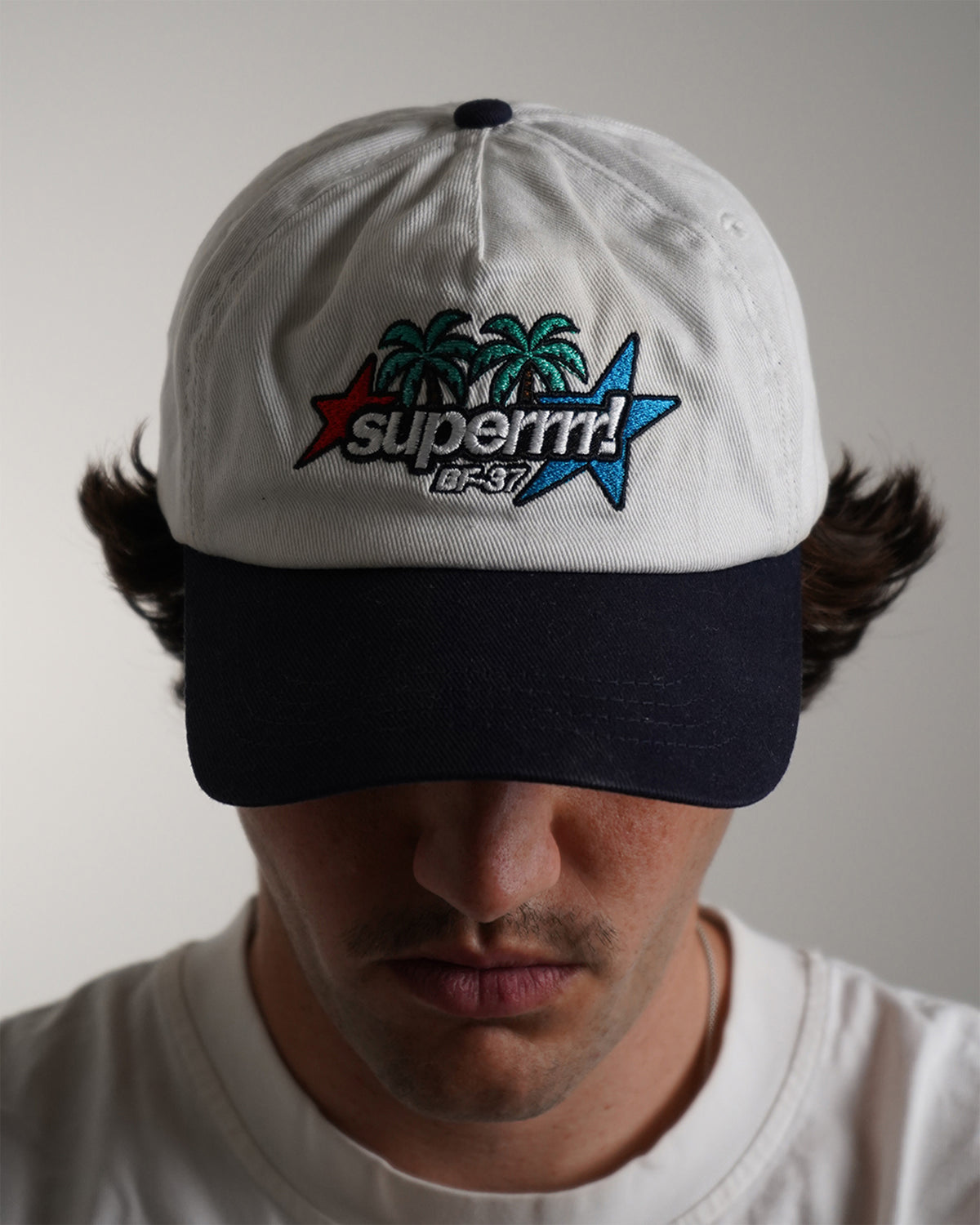 Front view modeled white Superrrr Hat with navy brim and embroidered palm trees, stars and superrrr! logo