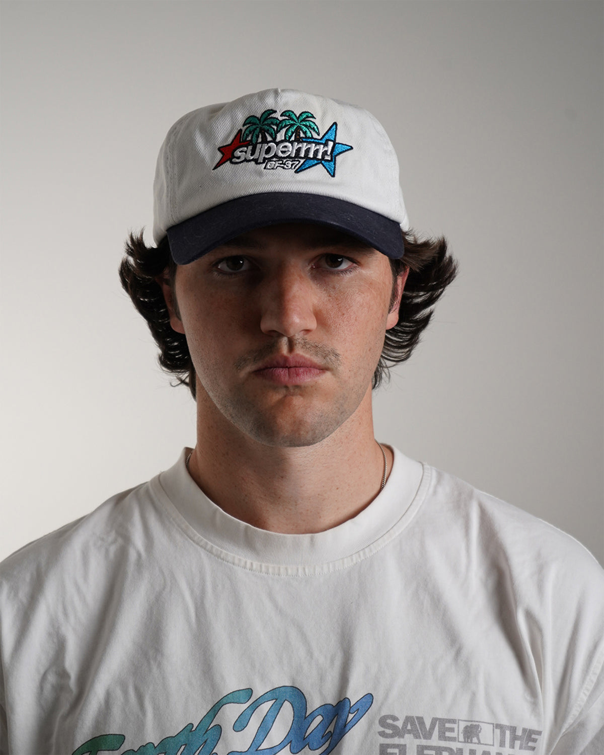 Front view modeled white Superrrr Hat with navy brim and embroidered palm trees, stars and superrrr! logo