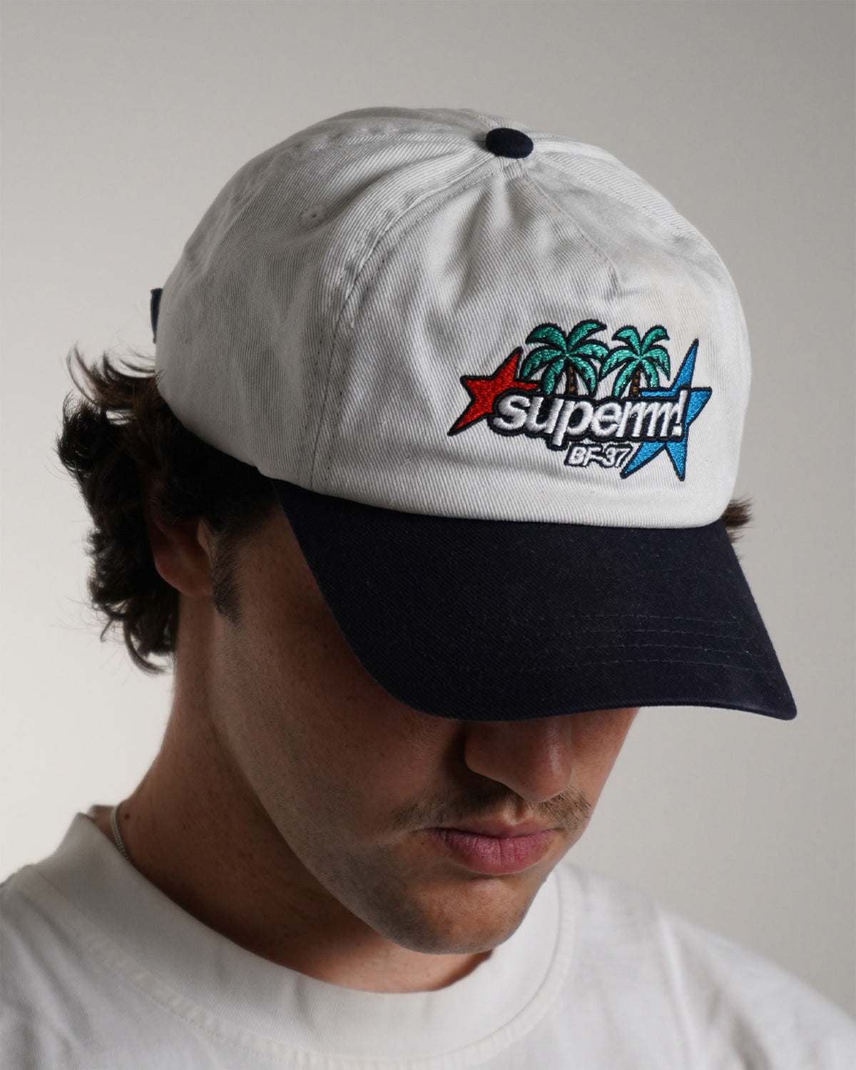 Front view modeled white Superrrr Hat with navy brim and embroidered palm trees, stars and superrrr! logo
