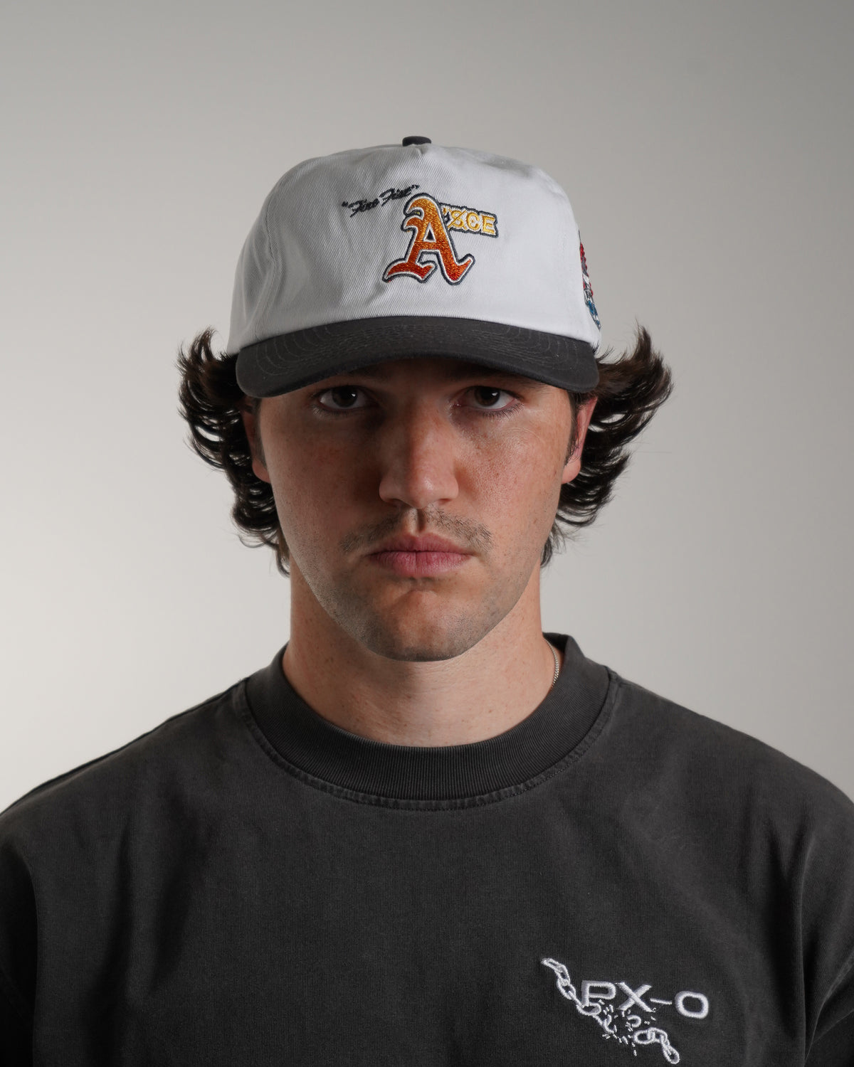 Model wearing the white Fire Fist Hat with black brim and an embroidered orange and yellow letter A graphic with script text, front view