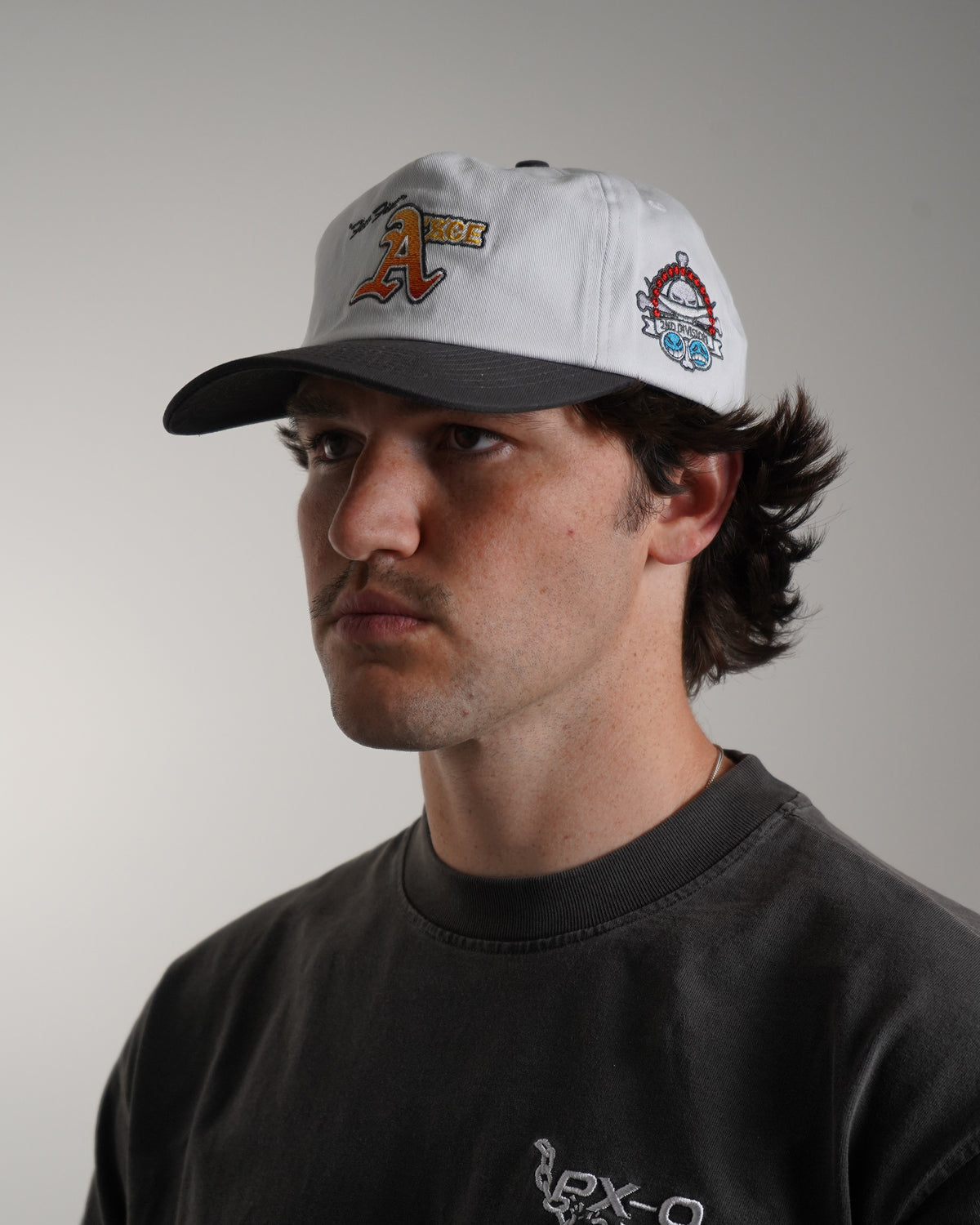 Side view on model of the white Fire Fist Hat with black brim, orange embroidered letter A with text, and round embroidered patch