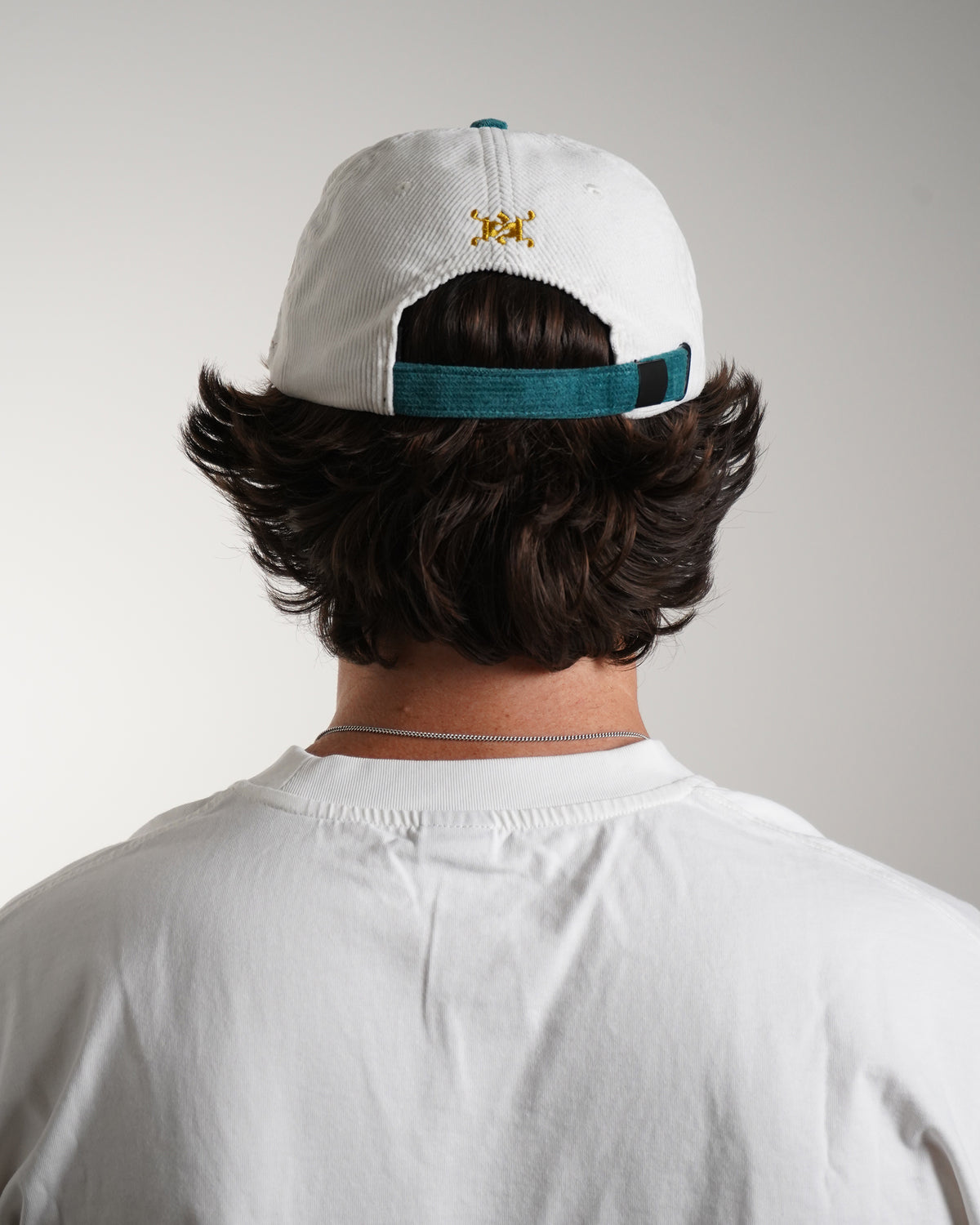 Back view on model of the white corduroy Rain Dinners Hat with teal strap and crown accent, small gold embroidered monogram above the strap