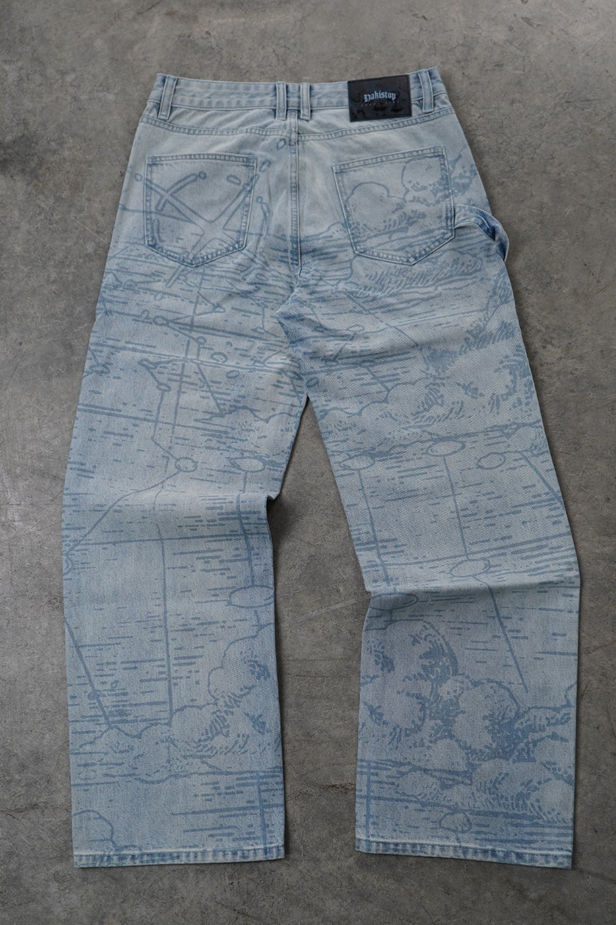 Back view flat lay of the light wash blue Grand Line Pants, wide-leg denim with an all-over blue map-like line graphic and a black leather patch at the waistband
