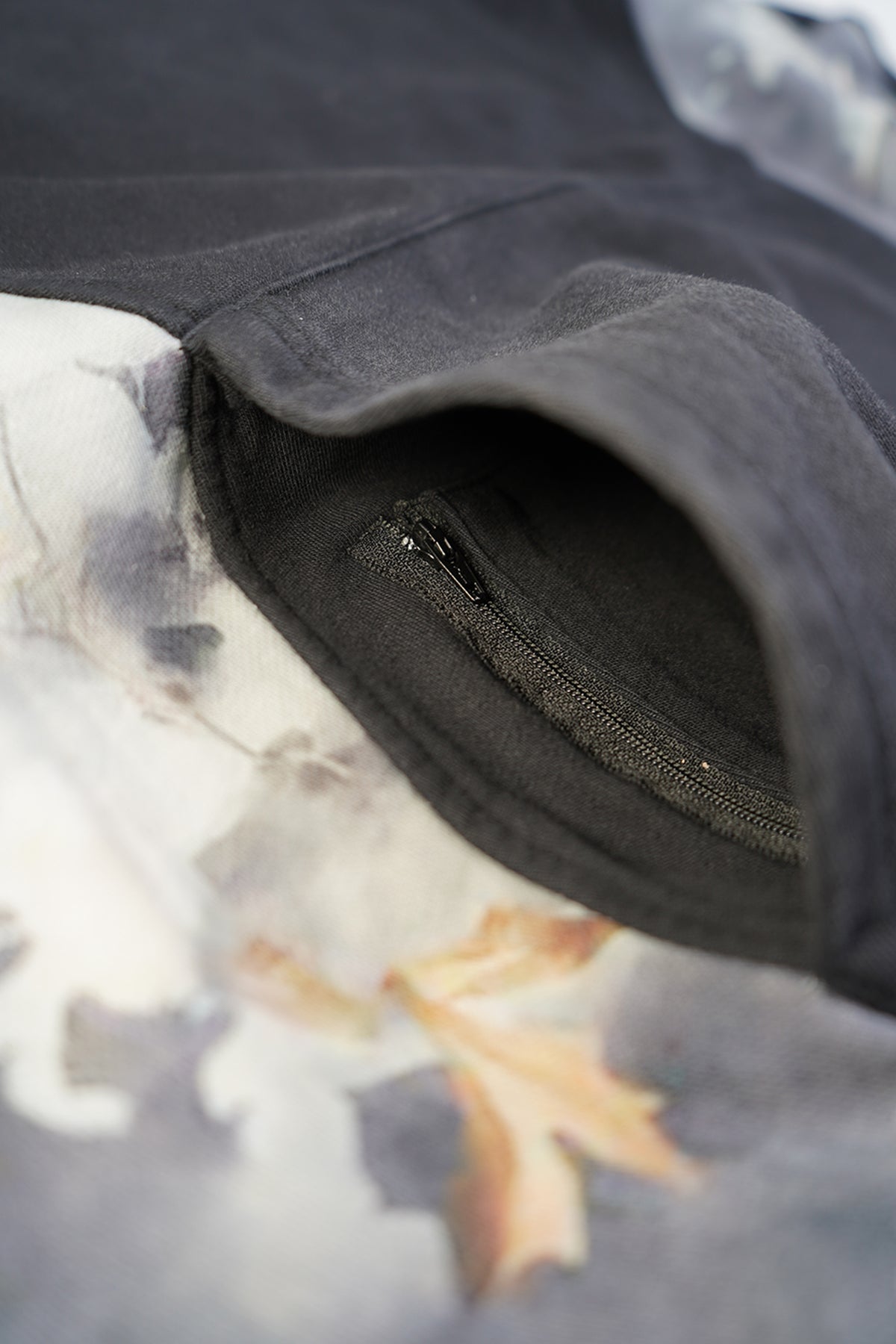 Close-up of the Hidden Inventory Hoodie black pocket opening with a small zippered pocket inside, beside a faded autumn leaf graphic