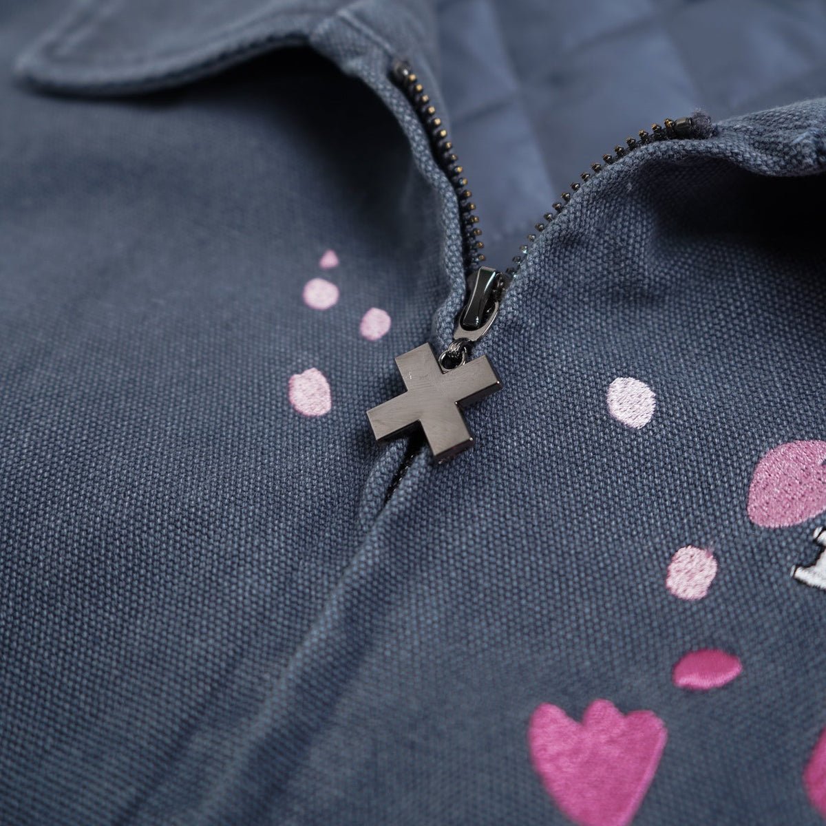 Close-up of a dark blue jacket with pink heart patterns and a cross pendant on a white background