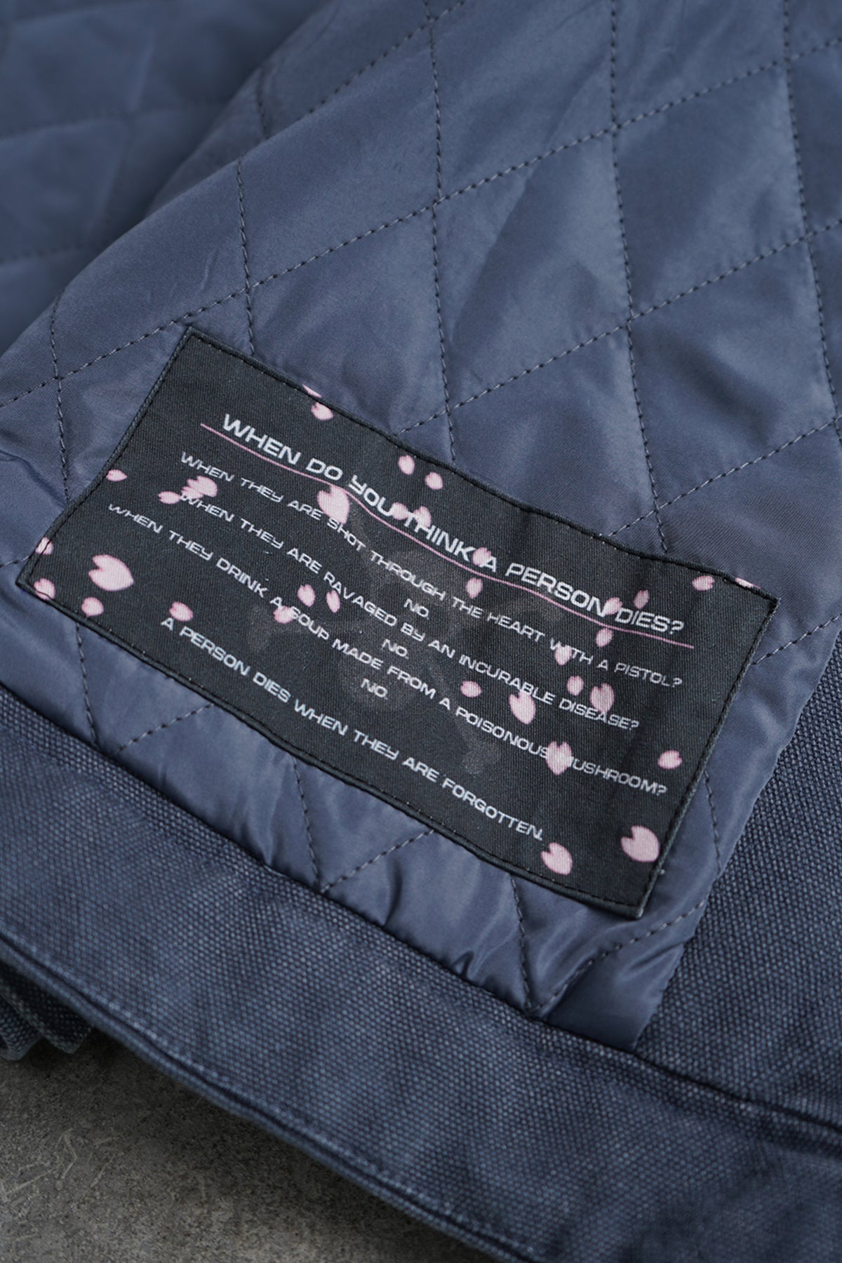 Close-up of a navy blue quilted fabric item with a black sewn-in label featuring white text and pink cherry blossom motifs.