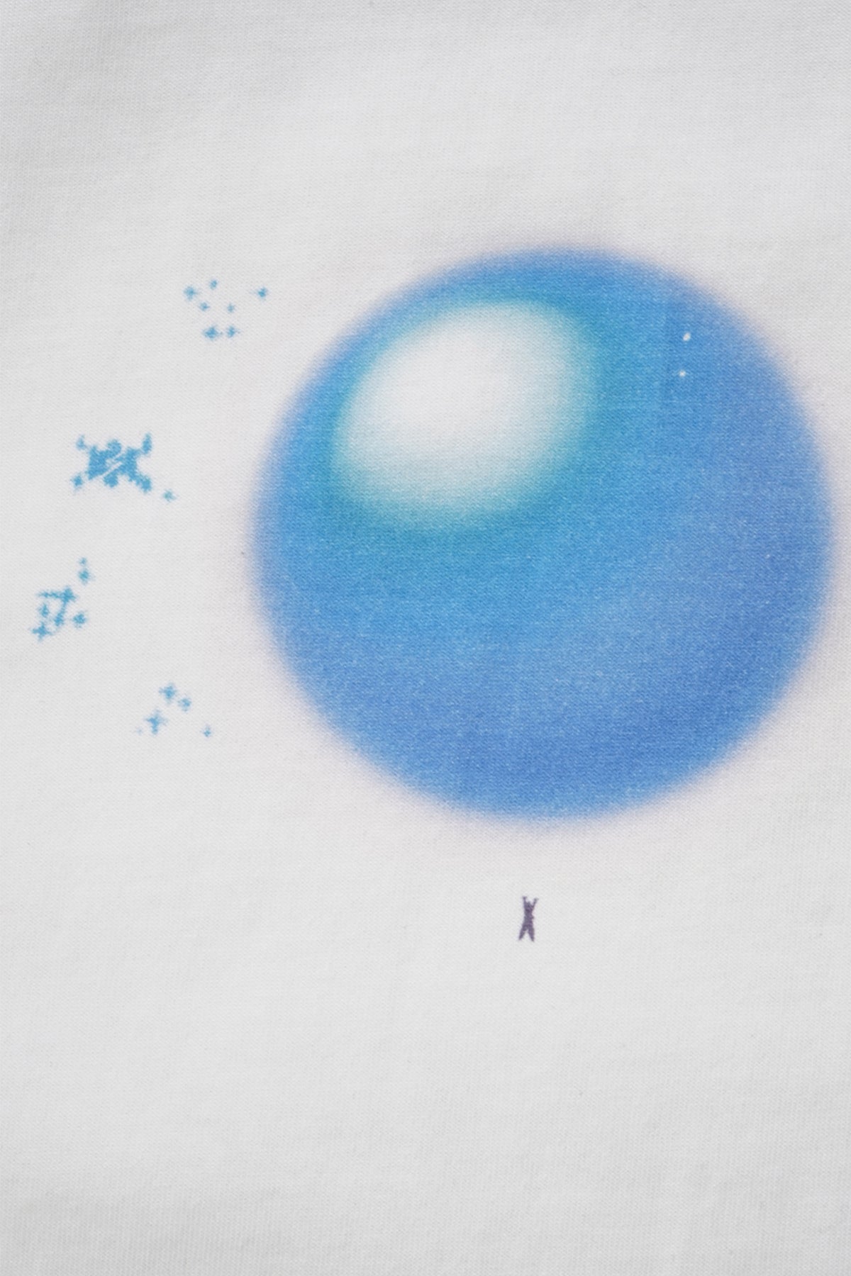 Close-up of the white Spirit Bomb Tee graphic: large blurry blue airbrushed orb with white highlight, tiny sparkles and a small figure below