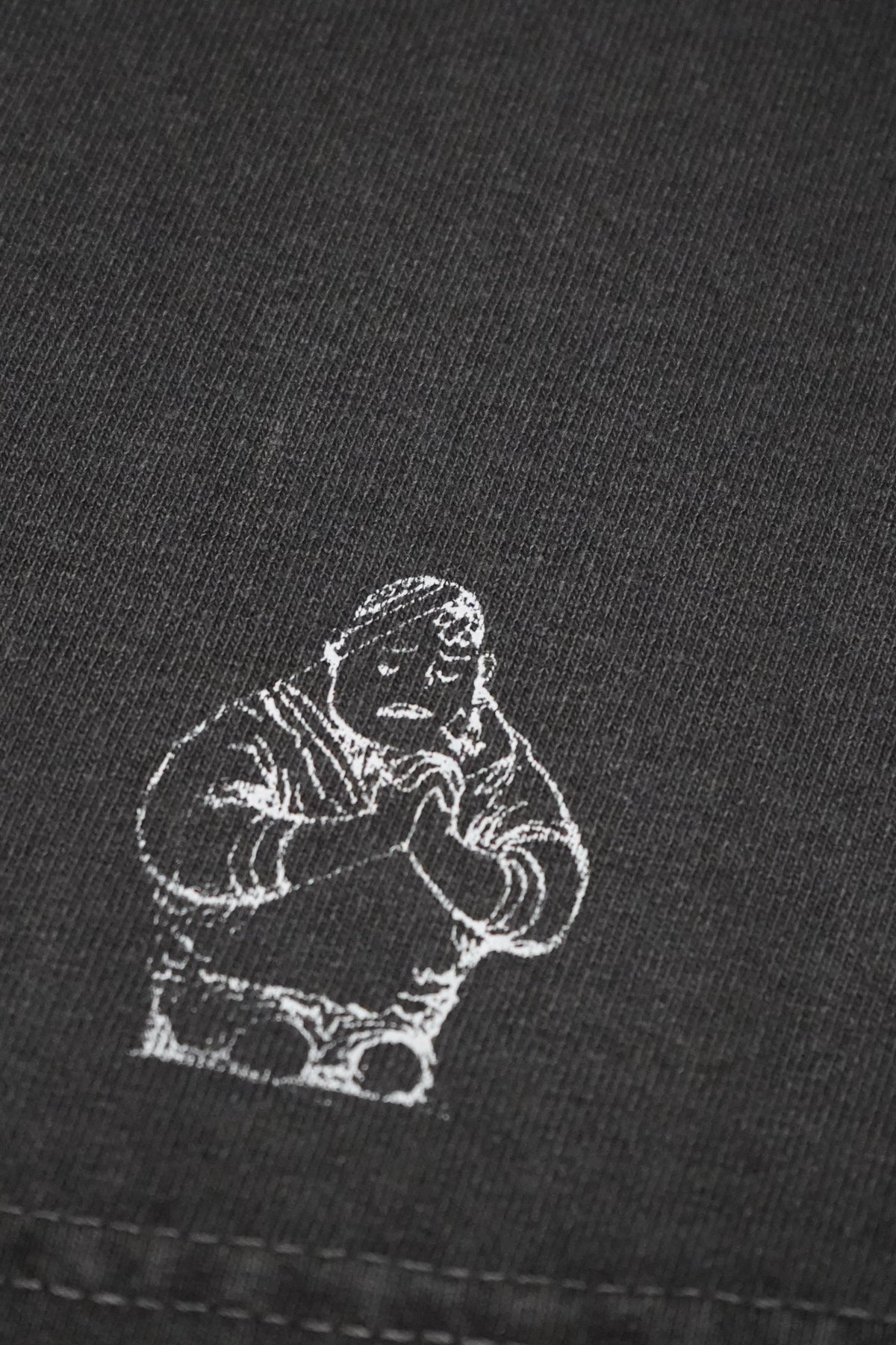 Close-up of a black knit garment featuring a small white printed graphic of a seated figure.