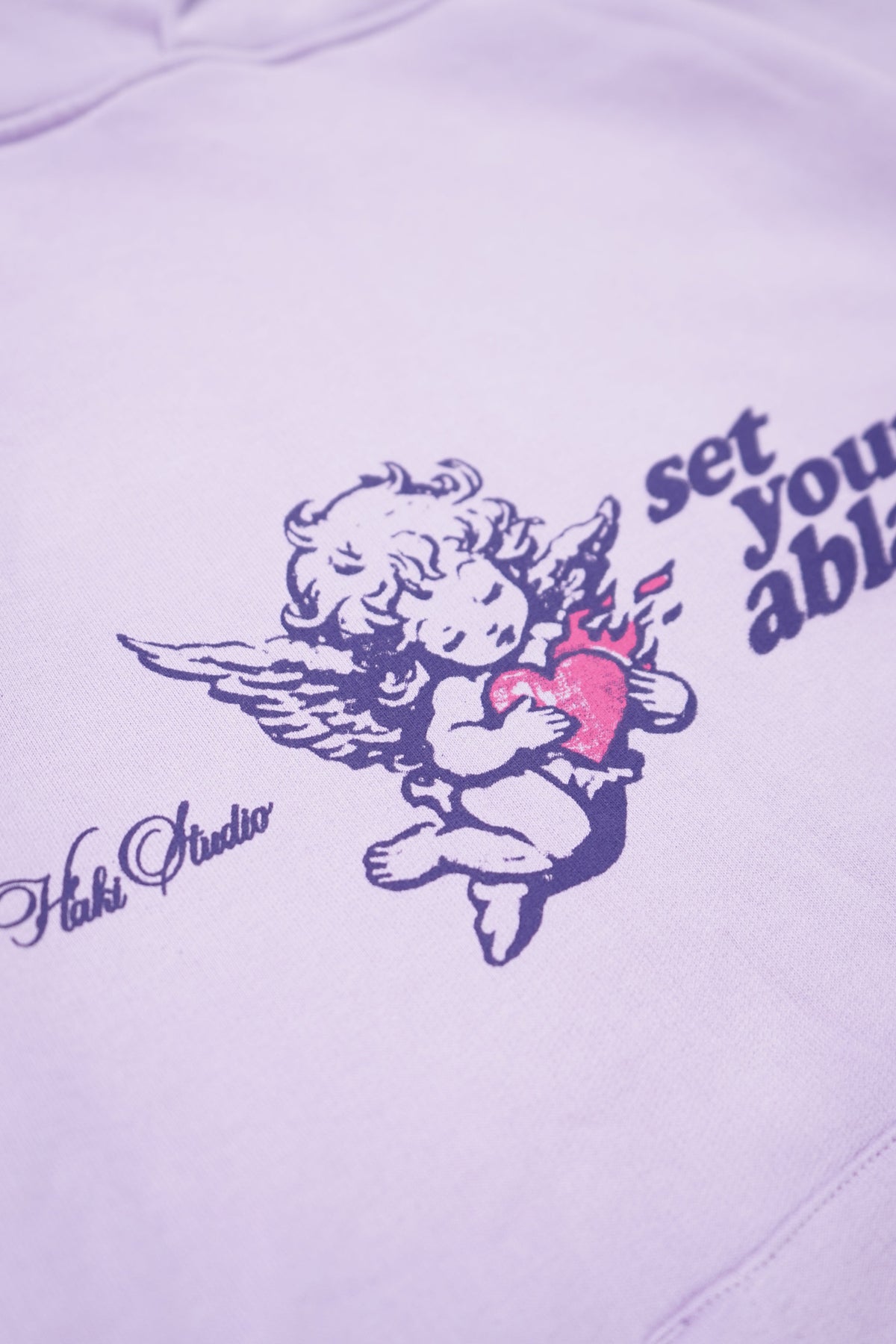 White sweatshirt with angel graphic and text on a light purple background