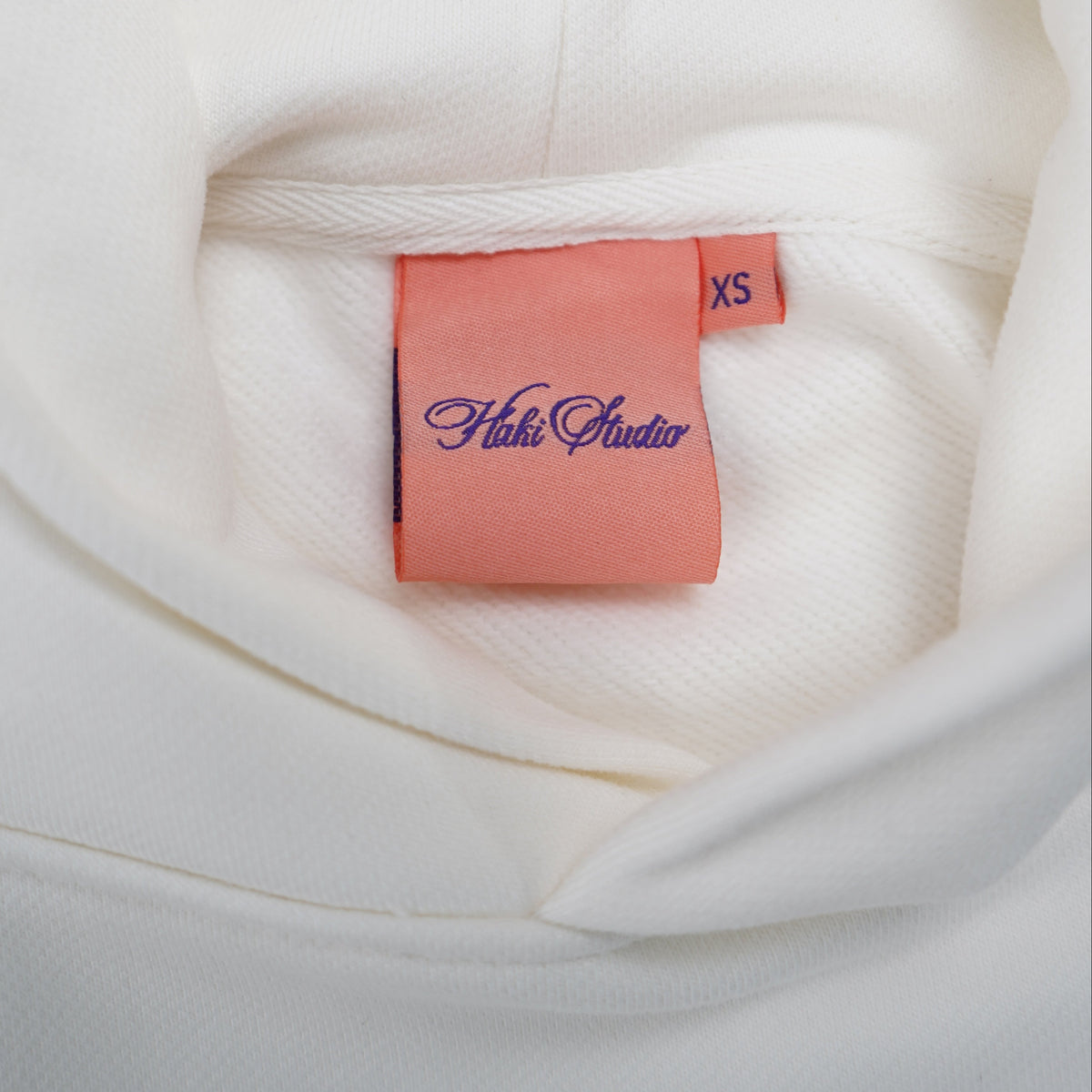 Close-up of a white garment with a pink label featuring 'Haki Studio' branding.