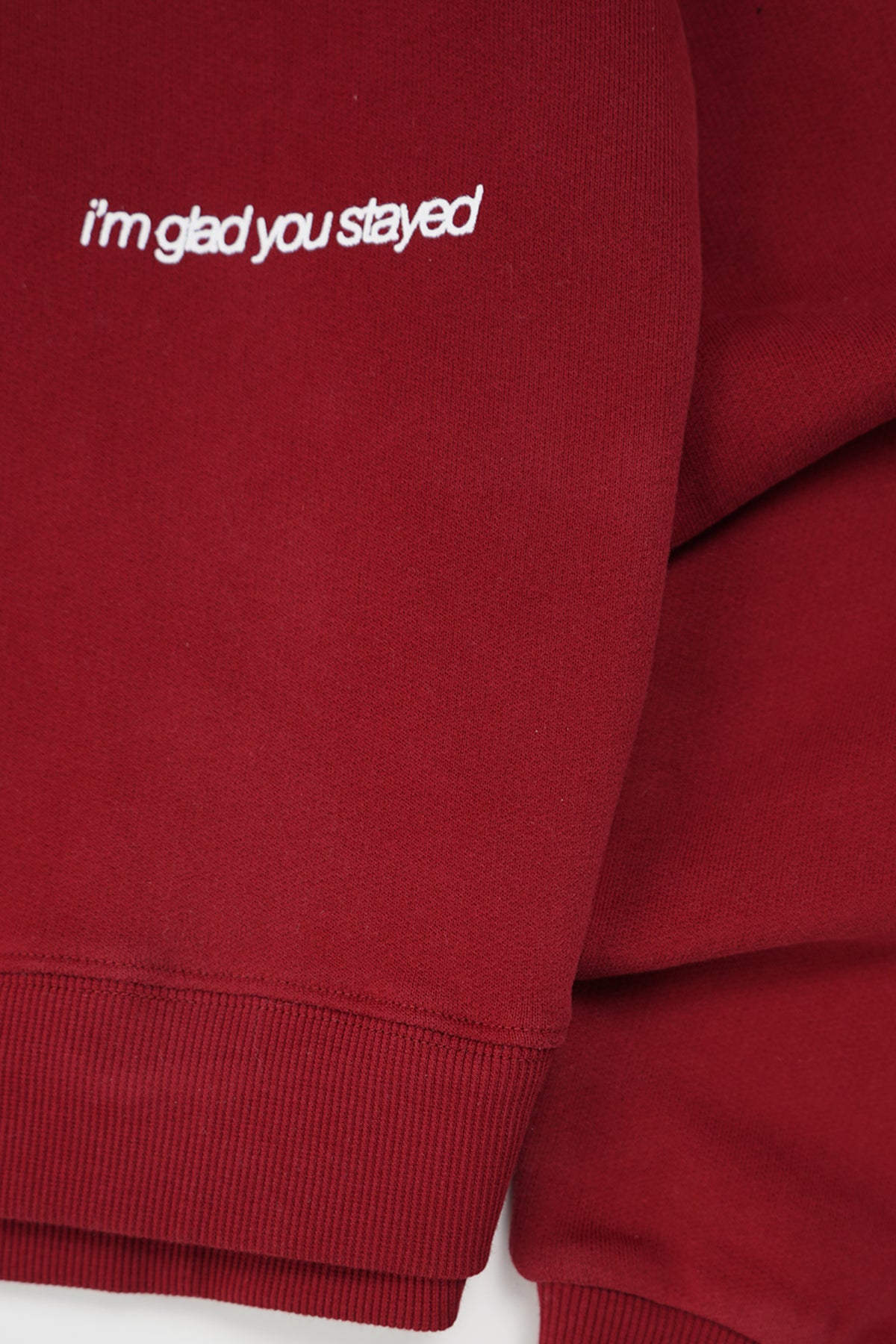 Close-up of the Cherry Red Come Over Hoodie sleeve with white embroidered text reading "i'm glad you stayed" above the ribbed cuff