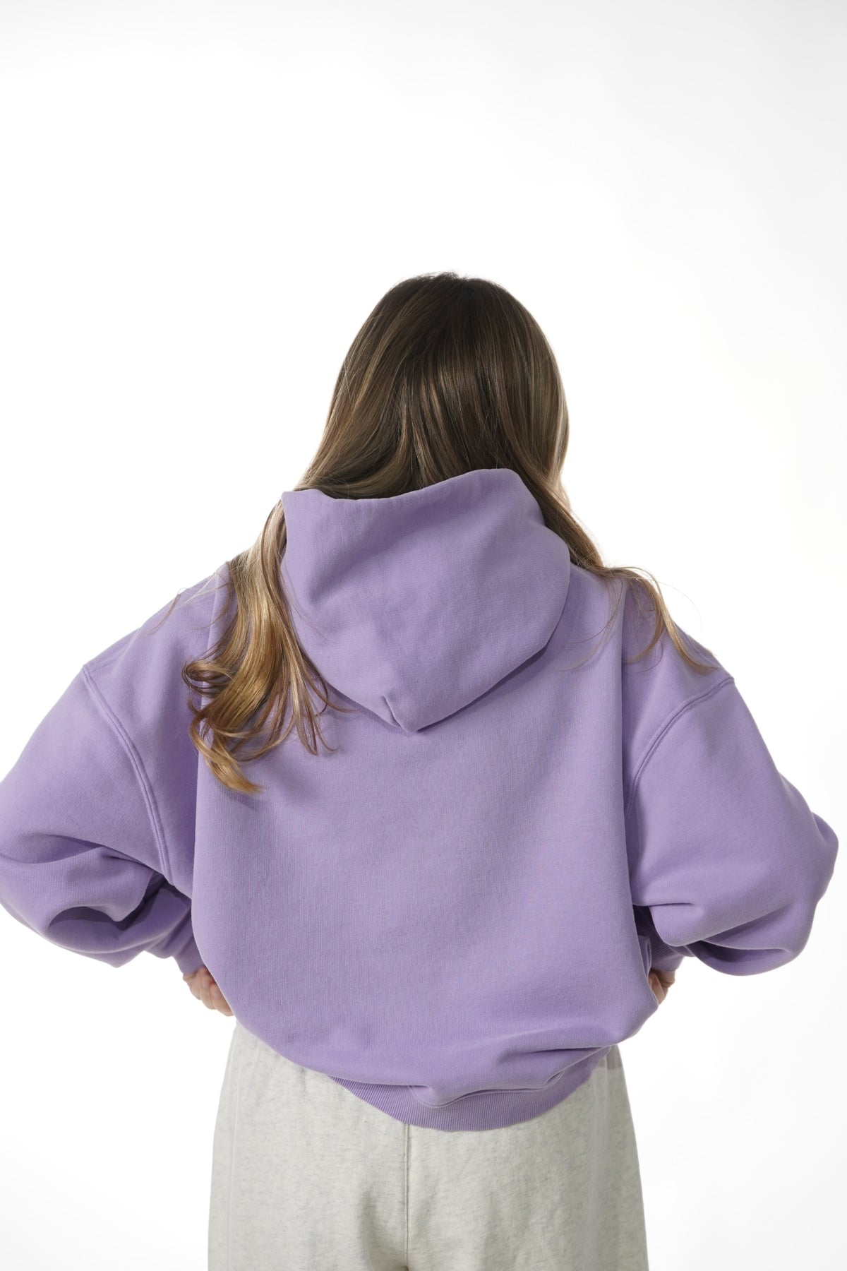 Person wearing a purple hoodie and gray pants on a white background