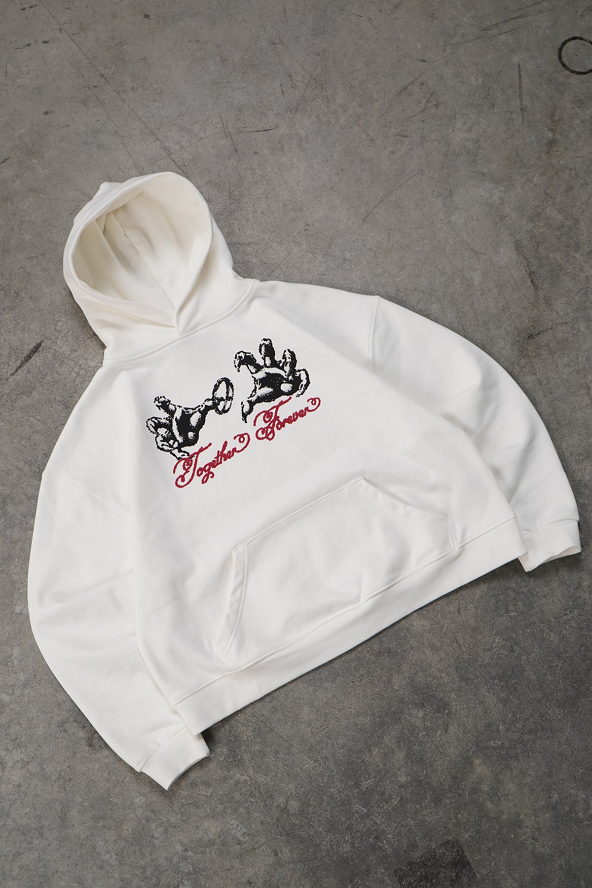 Flat lay of the cream white Together Forever Hoodie with front kangaroo pocket, black hands graphic and red cursive script text across the chest