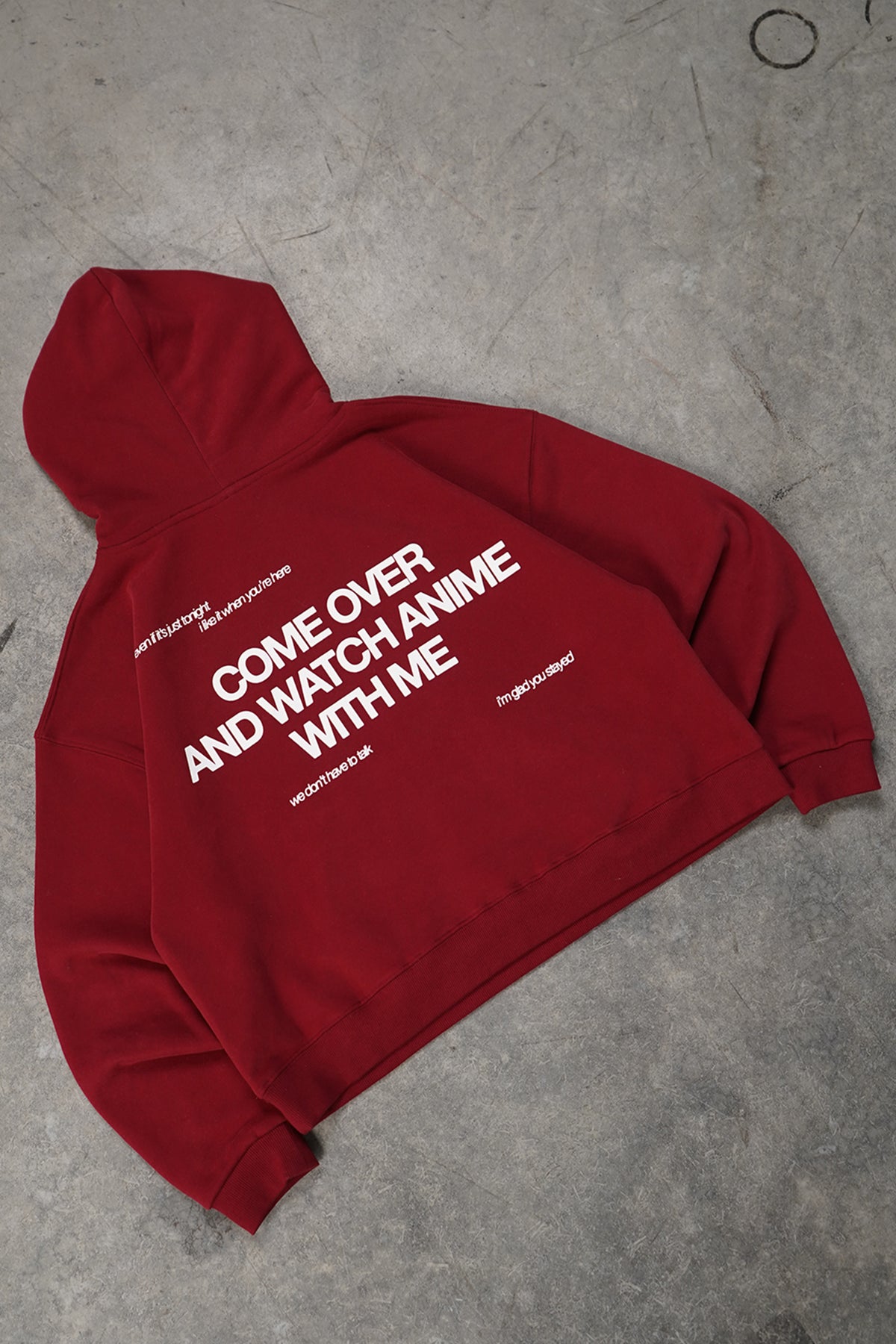 Flat lay back view of the Cherry Red Come Over Hoodie with large white printed text reading "COME OVER AND WATCH ANIME WITH ME" and smaller lines