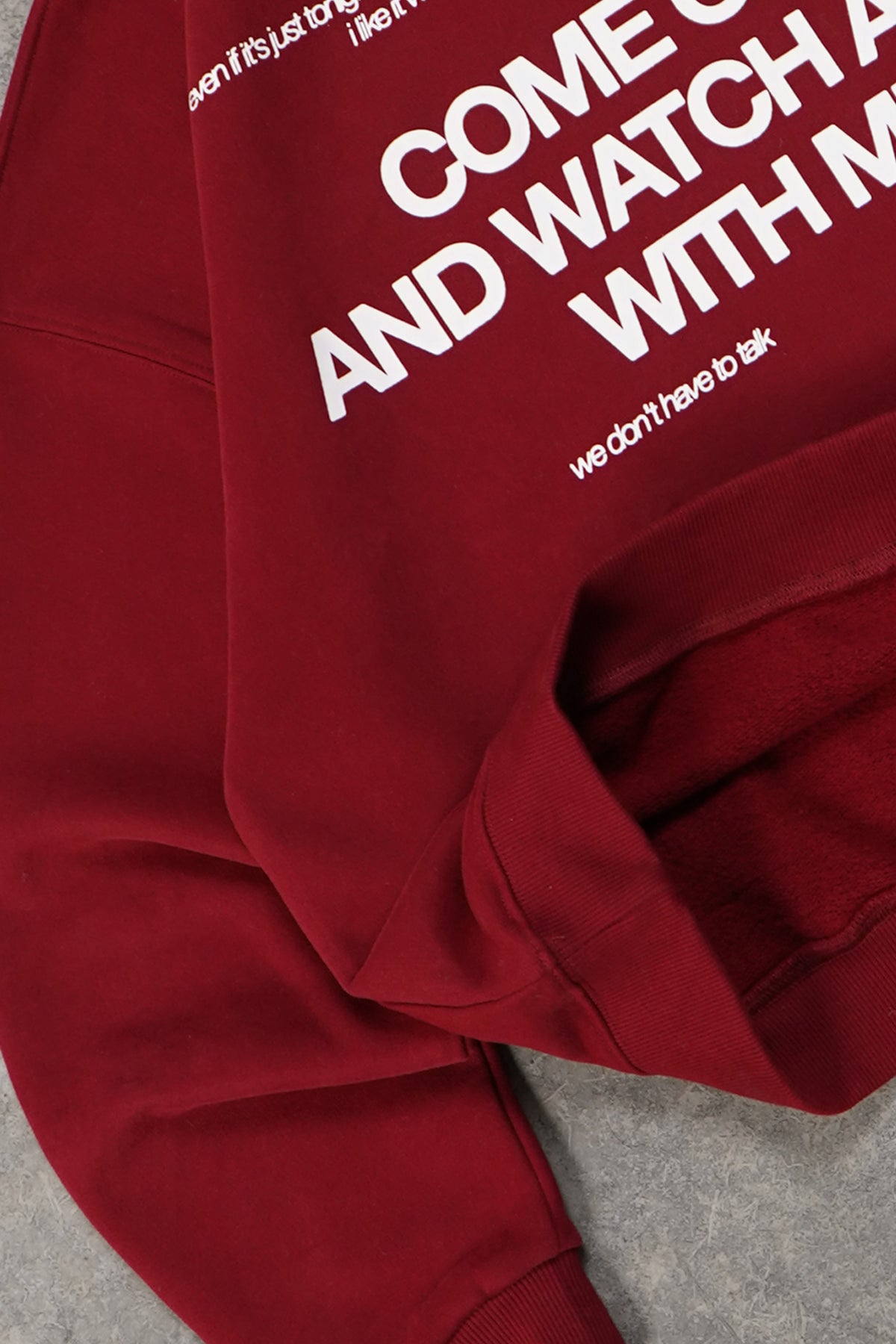 Close-up flat lay of the Cherry Red Come Over Hoodie sleeve and ribbed cuff, with partly visible white printed text in large and small lettering