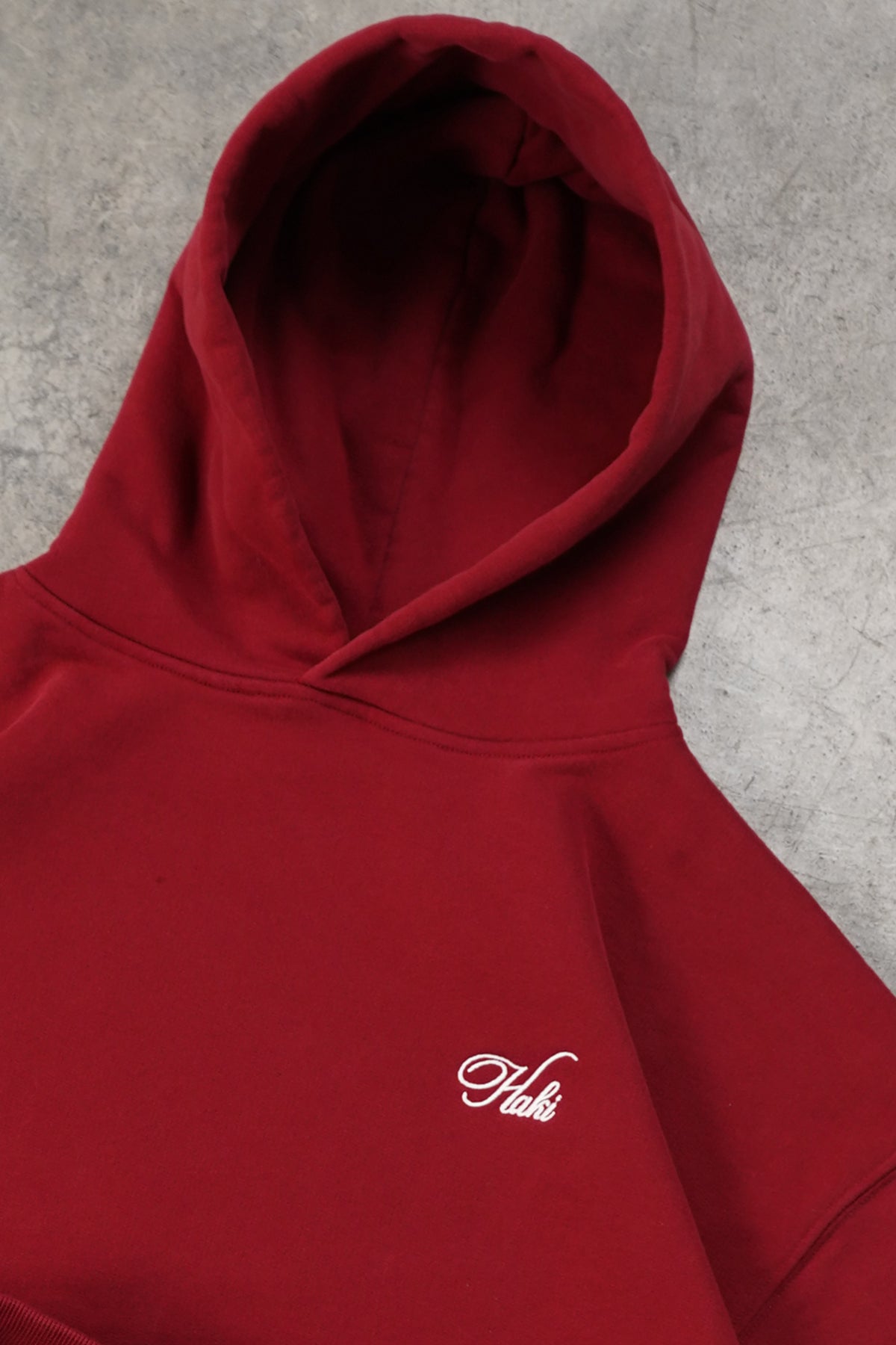 Flat lay close-up of the Cherry Red Come Over Hoodie showing the hood and small white embroidered script logo on the chest