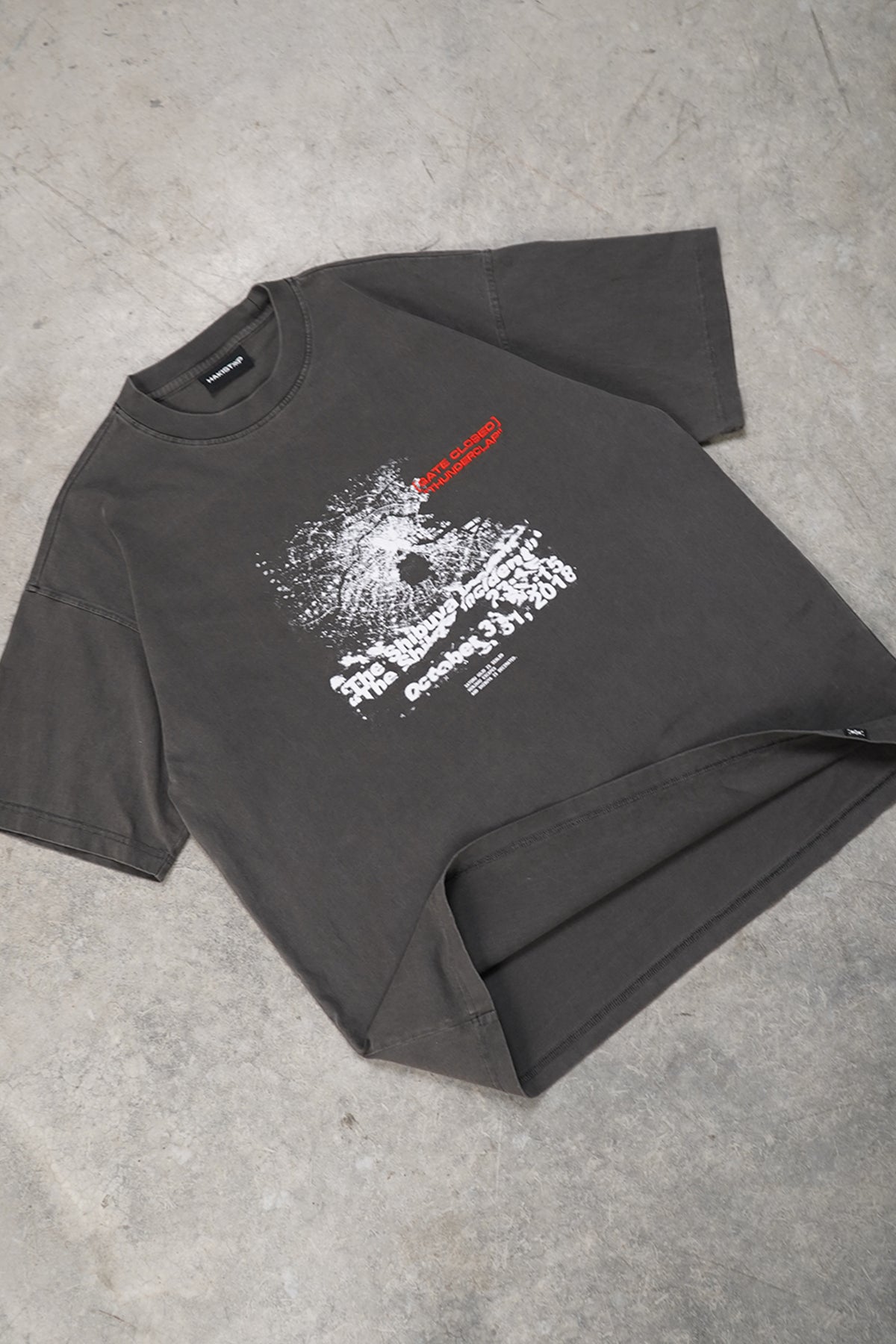 Flat lay of the faded charcoal grey Shibuya Incident Tee, front view, with a white cracked-glass style graphic, printed text and a small red text line on the chest