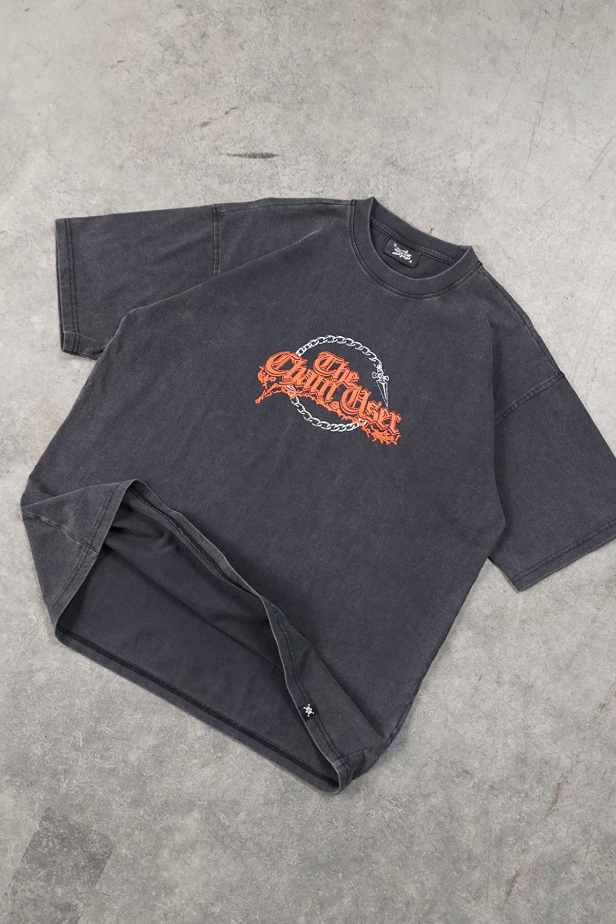 Flat lay of the faded black Chain User Tee, front view, with an orange gothic-lettered graphic inside a silver chain circle with a dagger