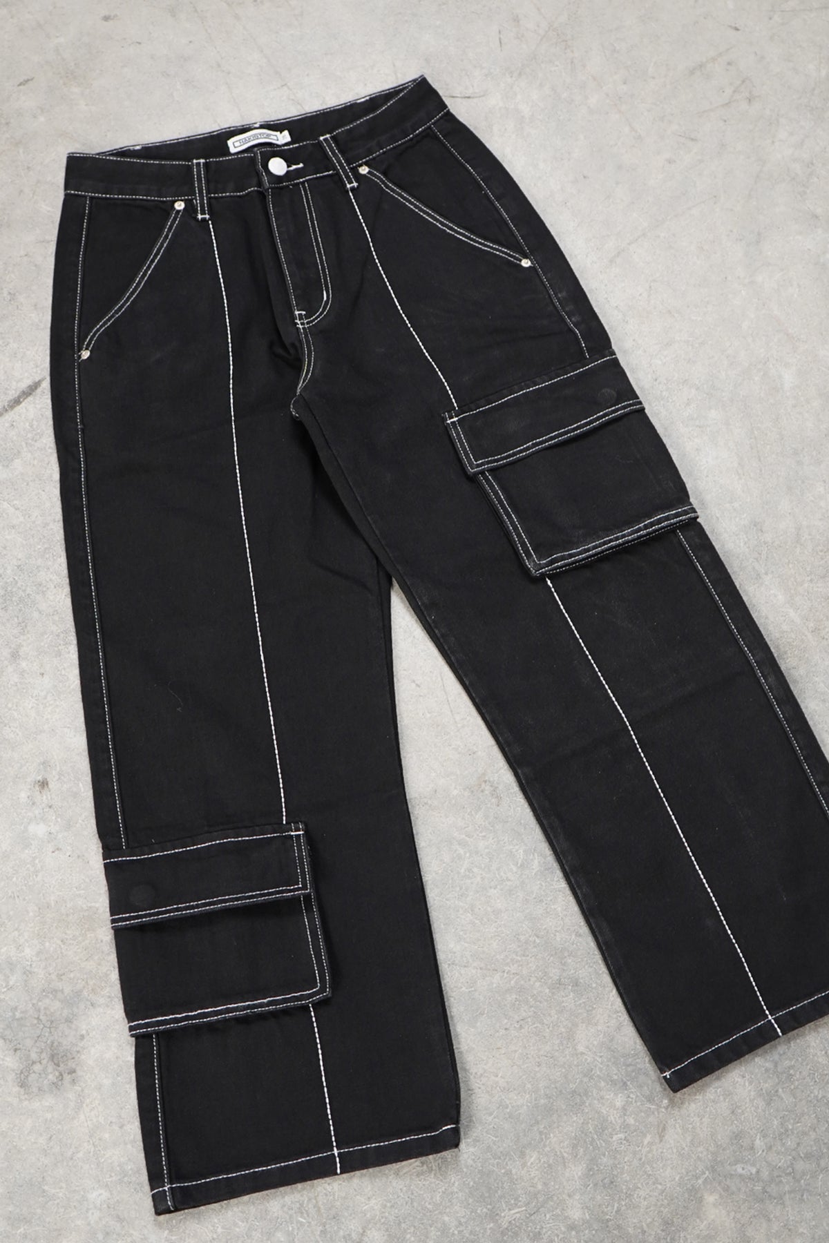 Flat lay of the black Divine Dogs Pants, wide-leg denim with white contrast stitching, side cargo flap pockets and a single waist button