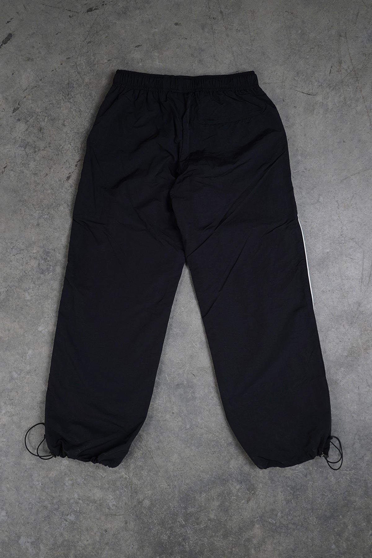 Flat lay of the black Jan-ken Trackpants, back view, with elastic waistband, back pocket, white side stripe and drawcord toggle hems