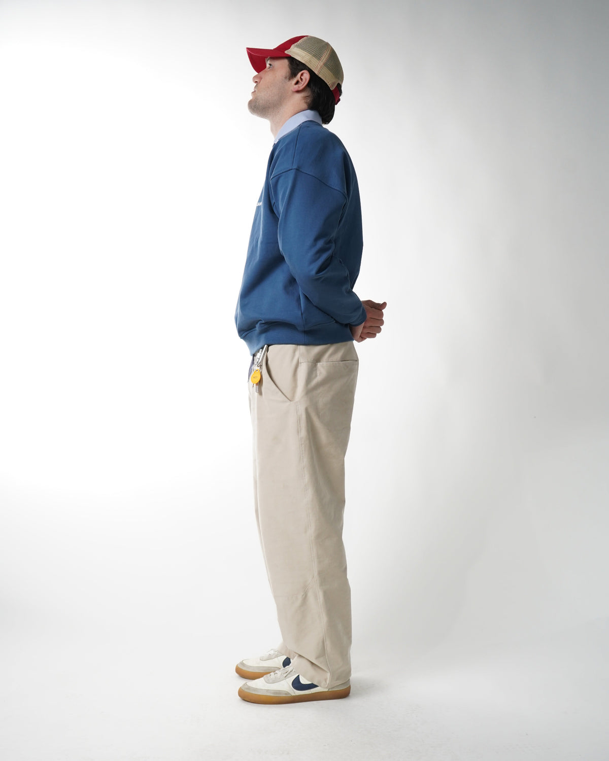 Person wearing a blue hoodie, beige pants, and a red and white cap on a white background
