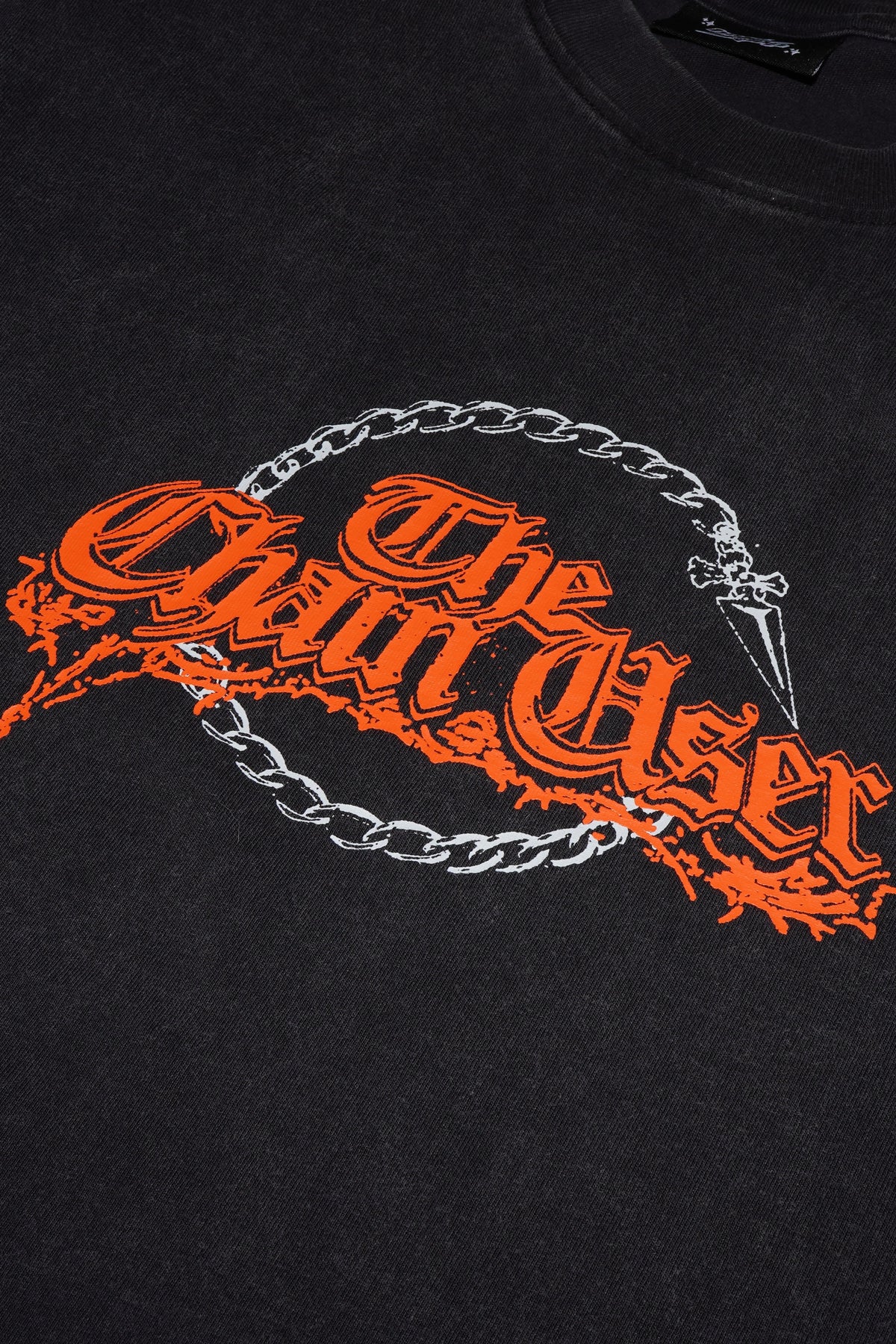 Close-up of a black t-shirt featuring a graphic print with the text 'The Chain User' in orange gothic lettering, overlaid with a silver chain and a small dagger motif.