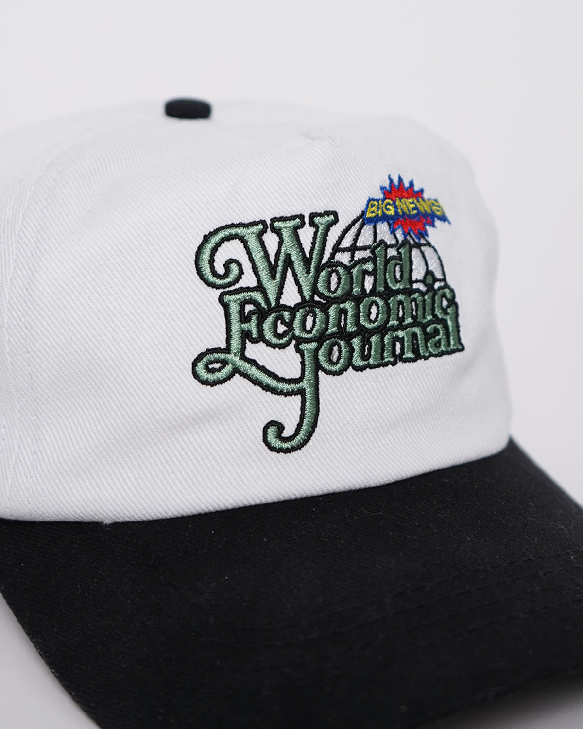 Close-up of the Big News! Hat, a white cap with black brim, showing green embroidered "World Economic Journal" lettering, a globe and a "Big News" burst